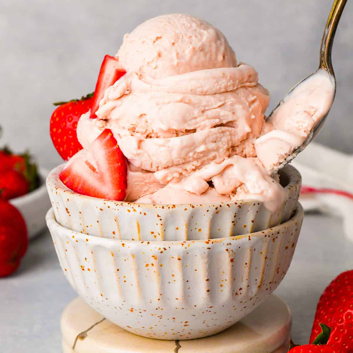 a bowl of strawberry ice cream with fresh strawberries and a spoon