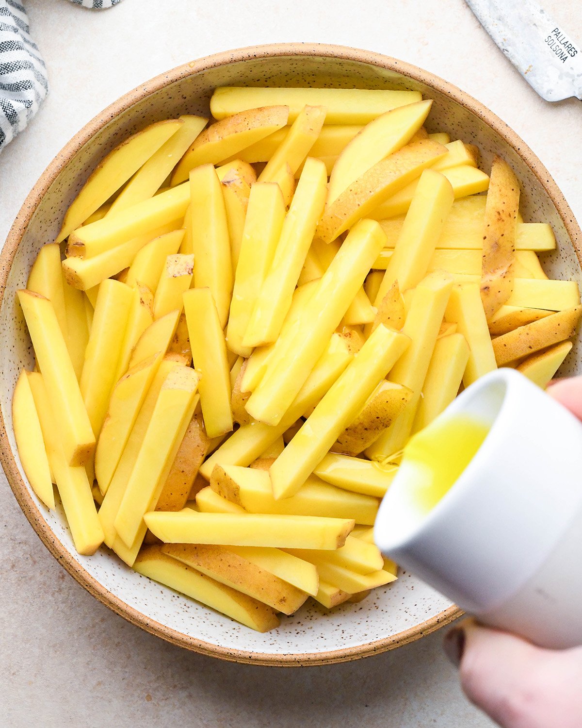 How to Make Homemade French Fries - pouring olive oil over potatoes