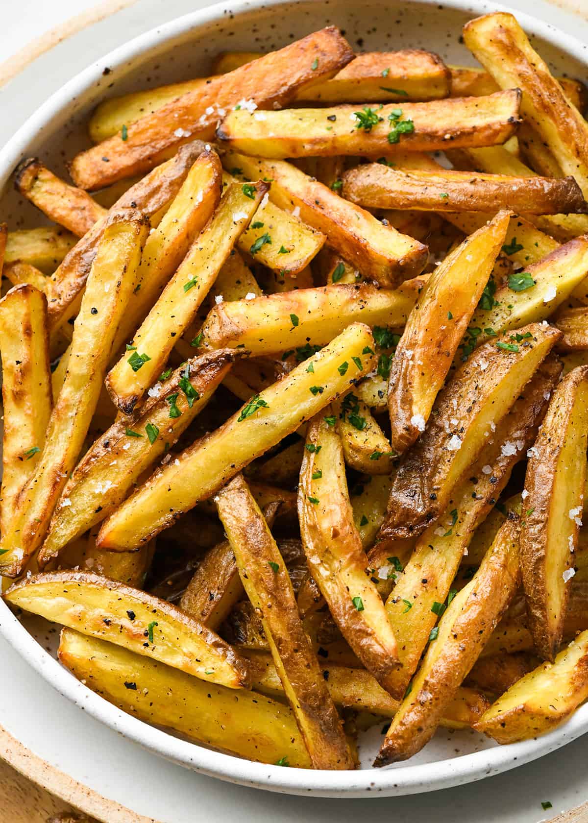 oven baked french fries in a bowl garnished with fresh parsley