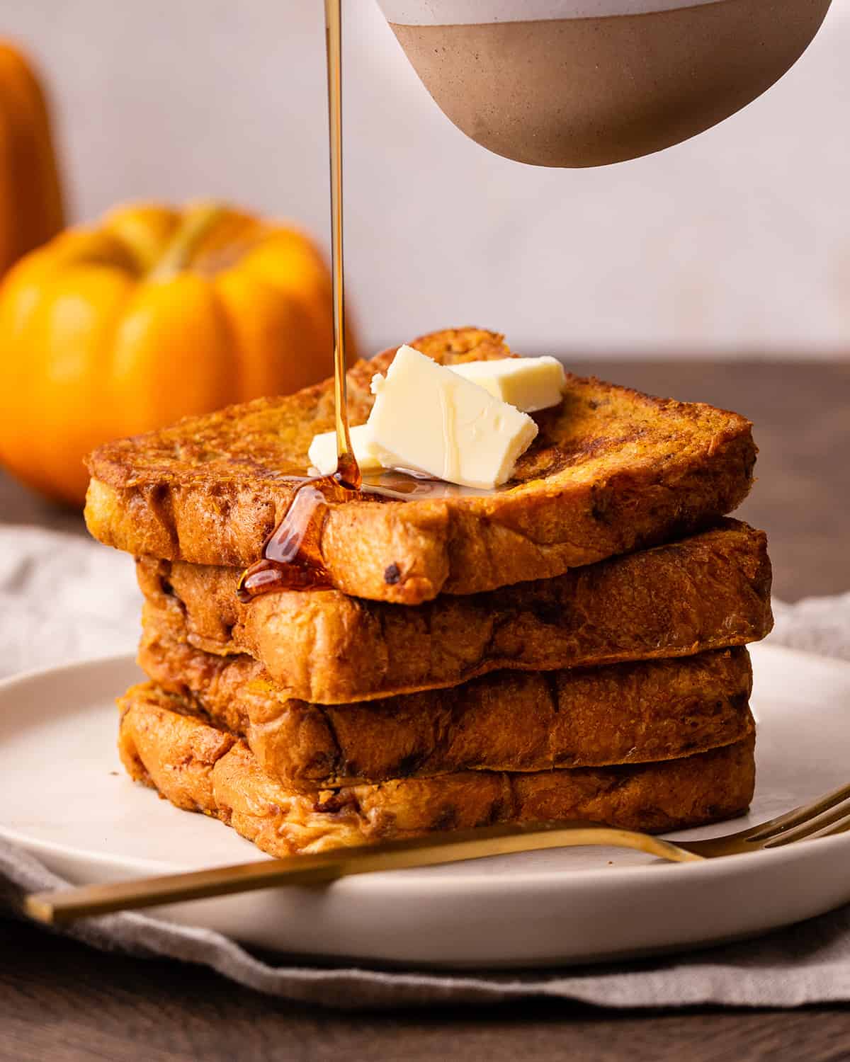 syrup being poured onto a stack of 4 pieces of Pumpkin French Toast with butter on top 