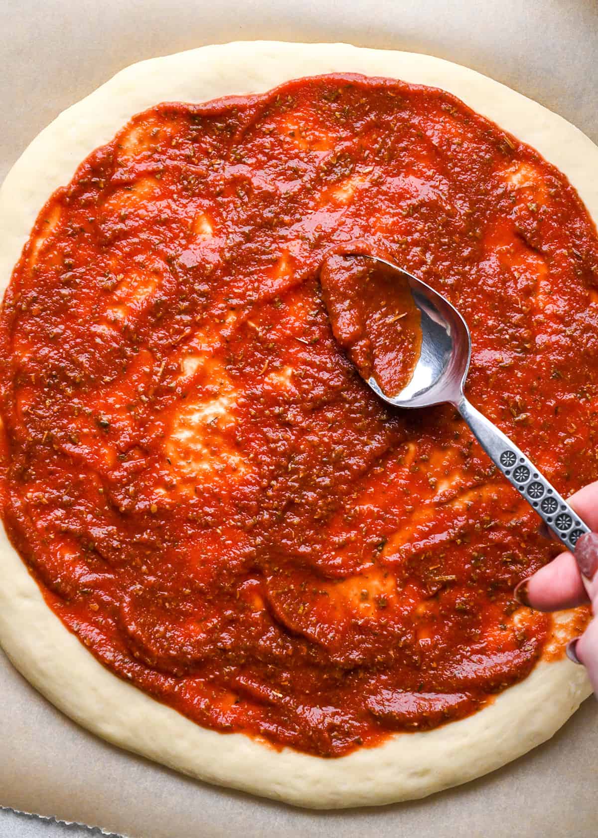 pizza sauce being spread on homemade pizza dough