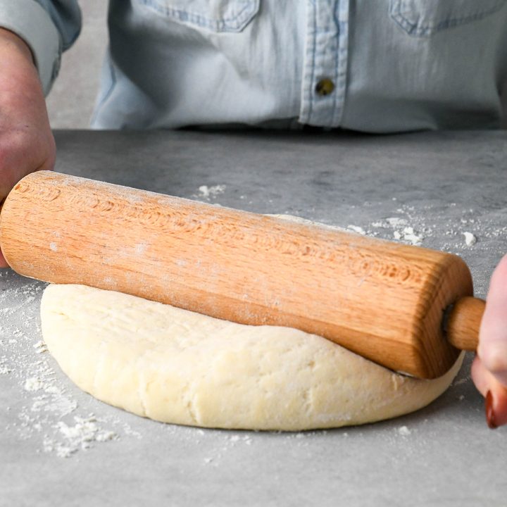 a woman rolling out pizza dough with a wooden rolling pin