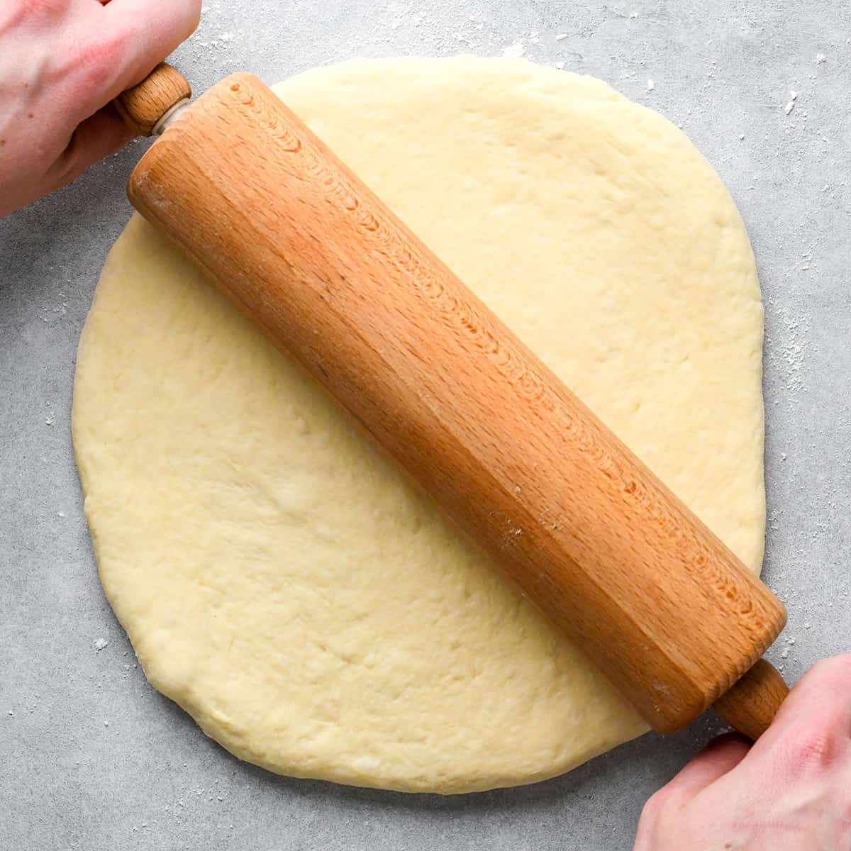 hands rolling out pizza dough with a wooden rolling pin
