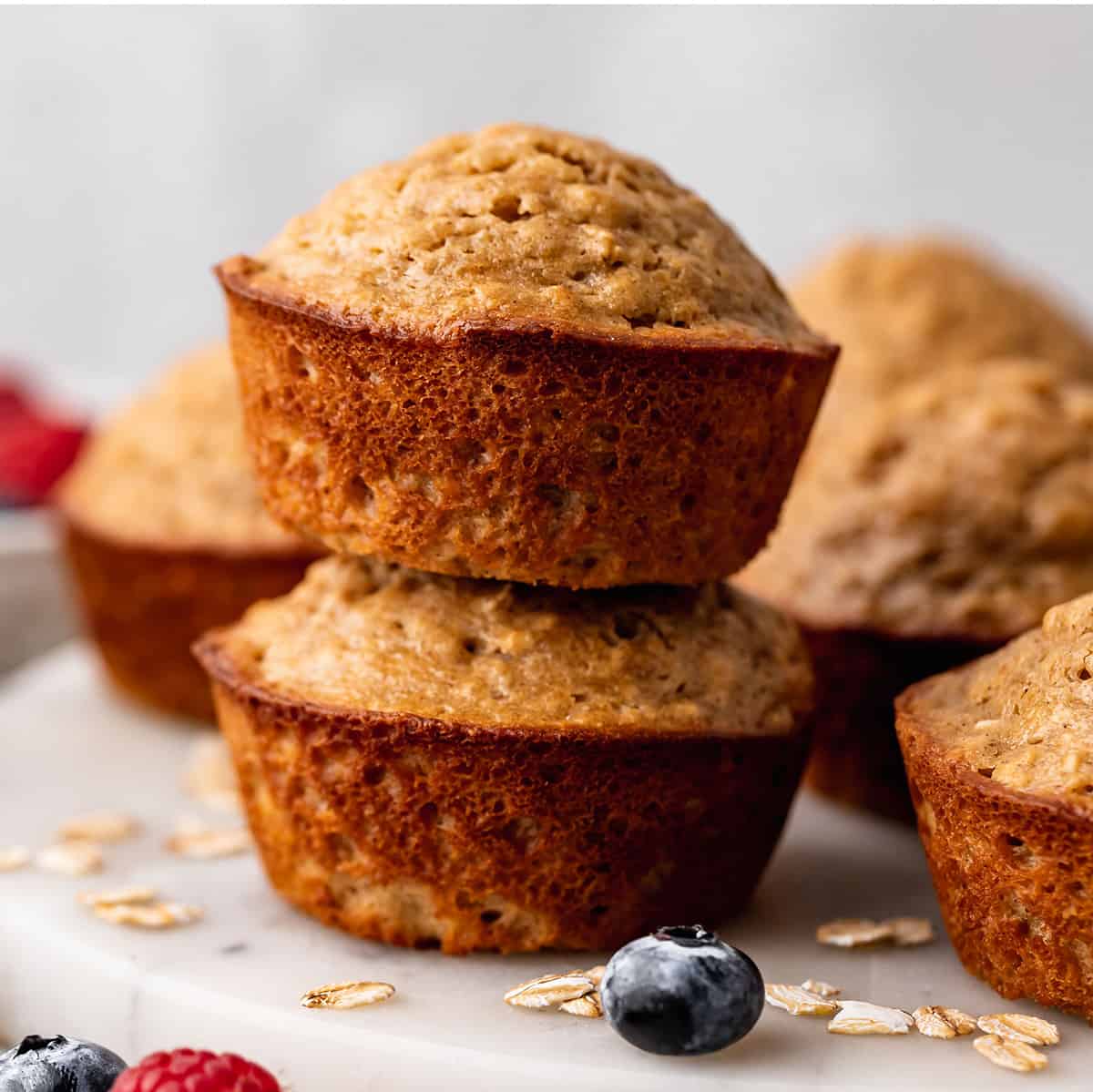 a stack of 2 Oatmeal Muffins surrounded by other muffins & berries