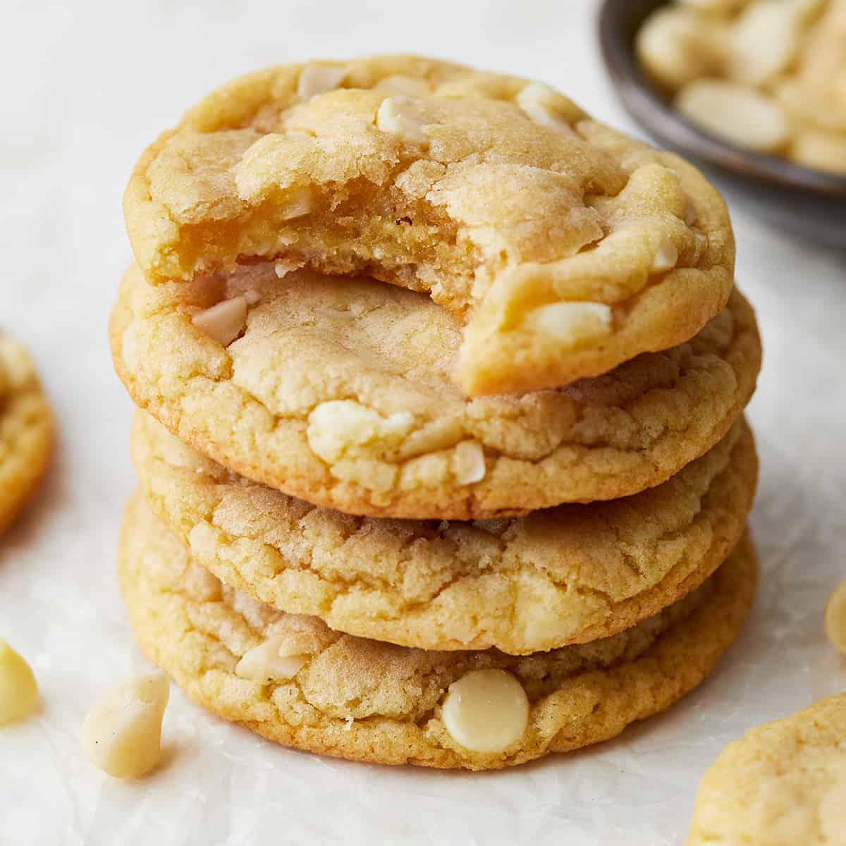 a stack of 4 White Chocolate Macadamia Nut Cookies, the top one has a bite taken out of it
