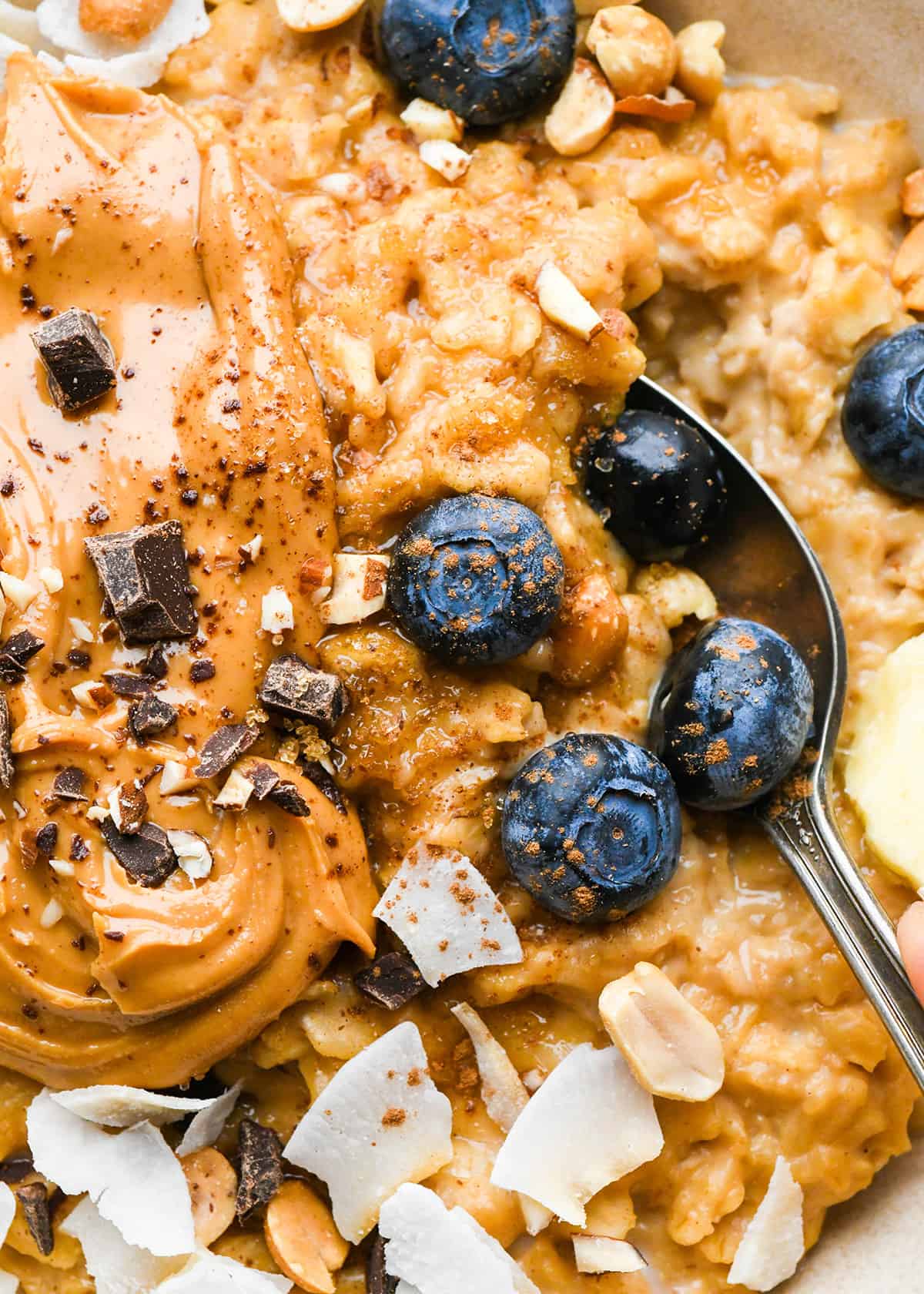up close photo of a spoon taking a scoop of Peanut Butter Oatmeal in a bowl topped with blueberries and other toppings
