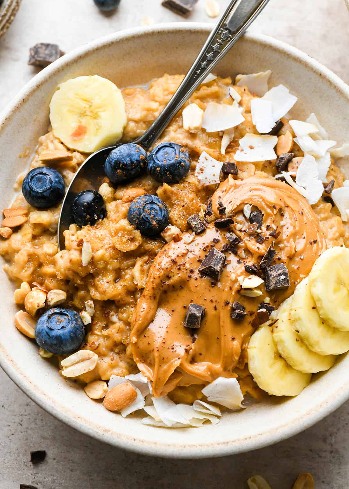 a bowl of Peanut Butter Oatmeal topped with blueberries, bananas, peanut butter, chocolate and coconut