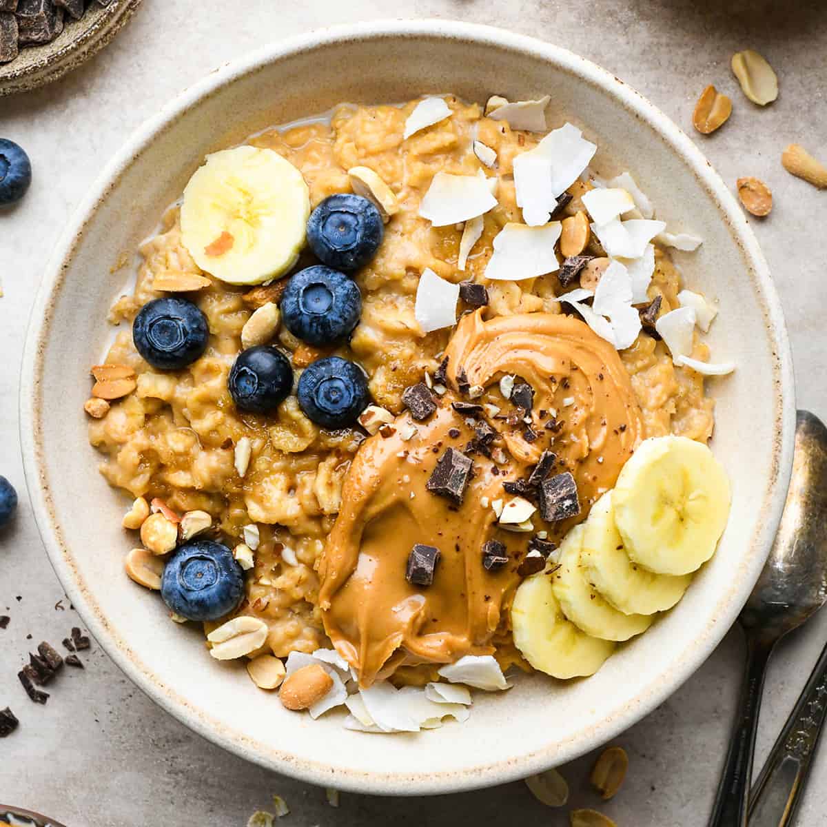 a bowl of Peanut Butter Oatmeal topped with blueberries, bananas, peanut butter, chocolate and coconut
