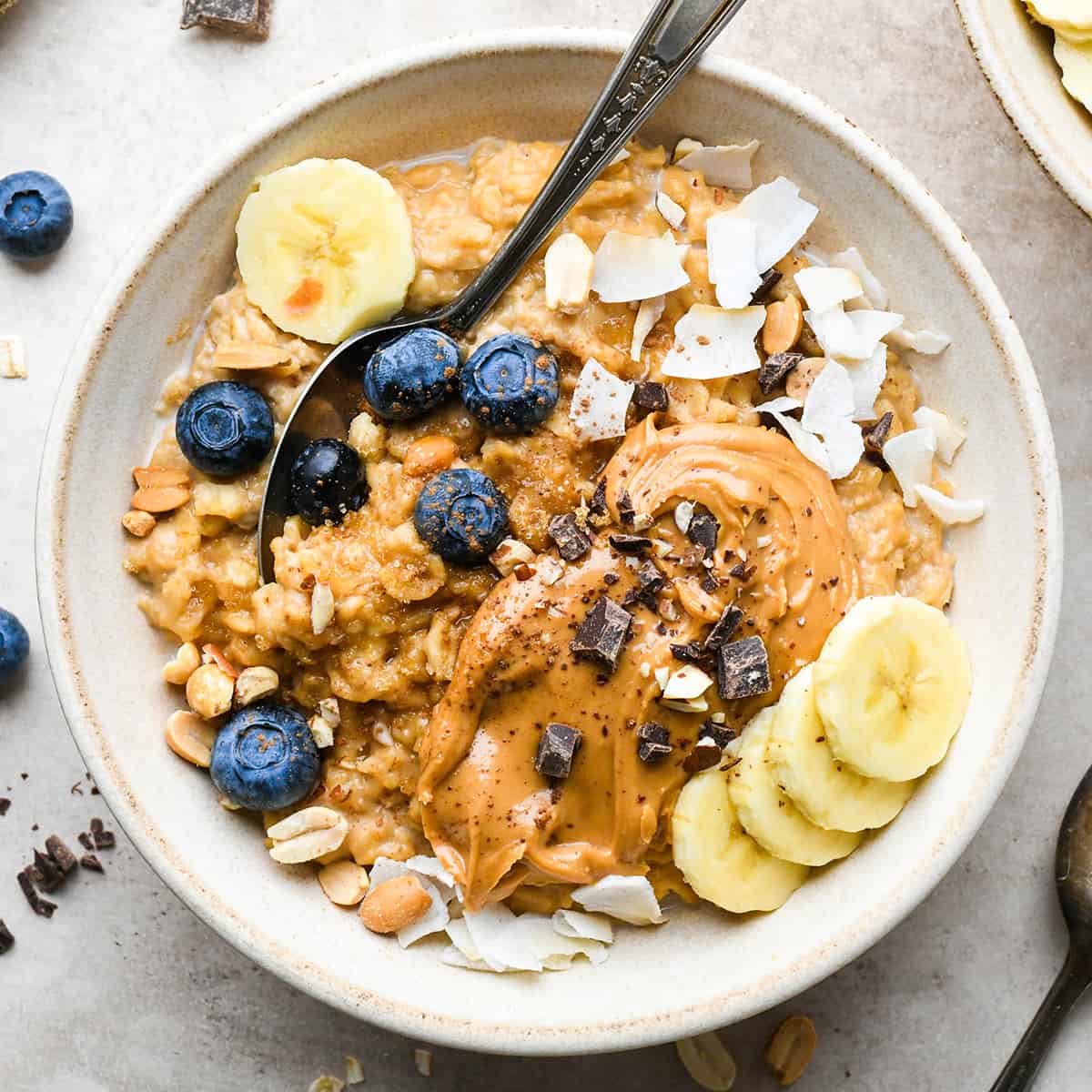 Peanut Butter Oatmeal in a bowl with a spoon and toppings like blueberries and bananas. 