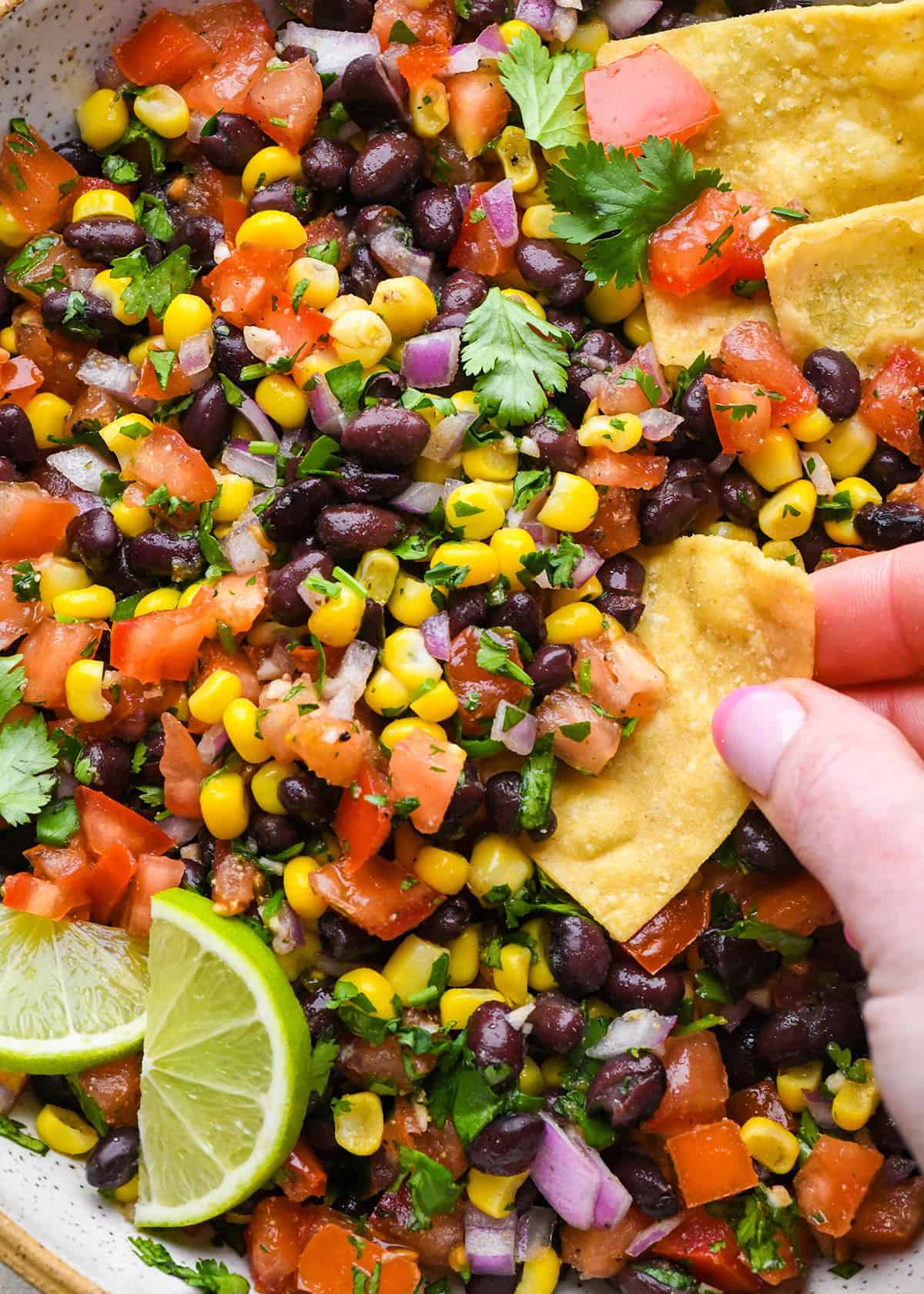 up close photo of a hand dipping a chip into Black Bean and Corn Salsa