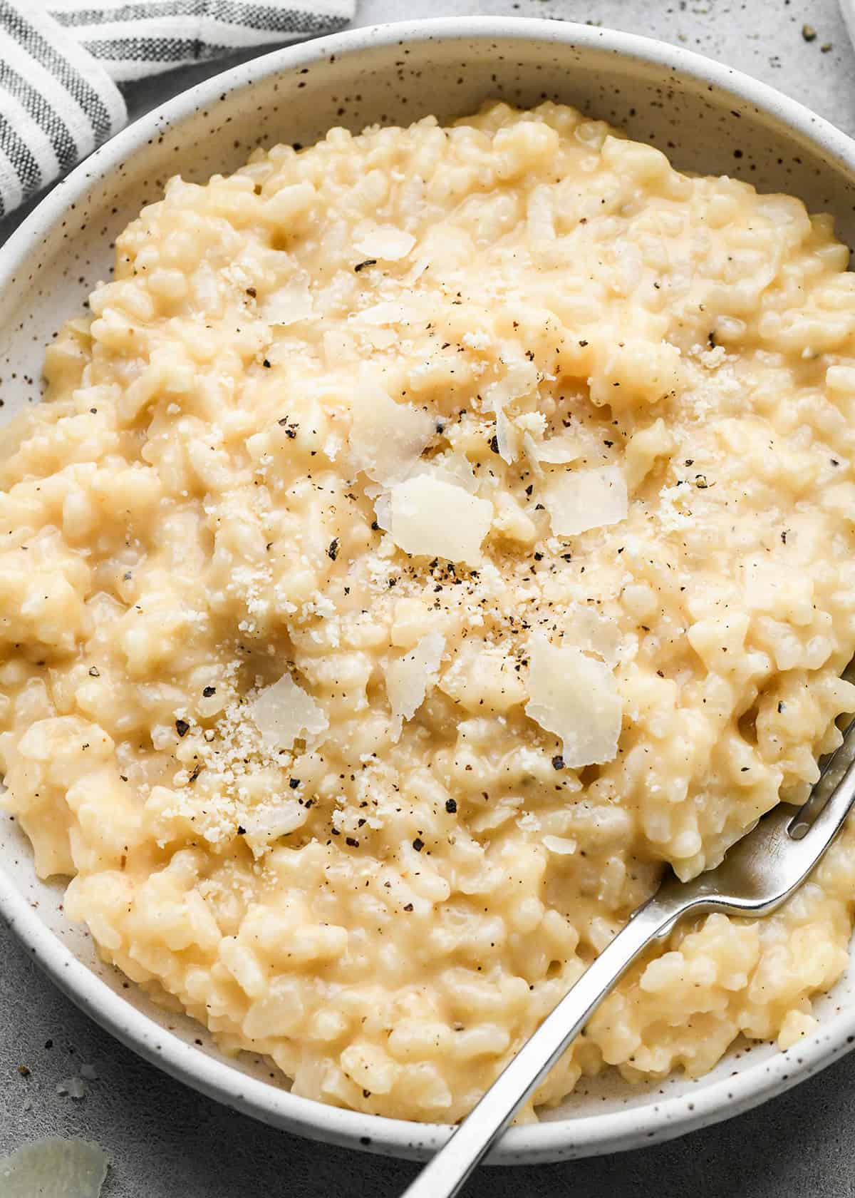 a bowl of risotto with a fork topped with parmesan cheese, salt and pepper