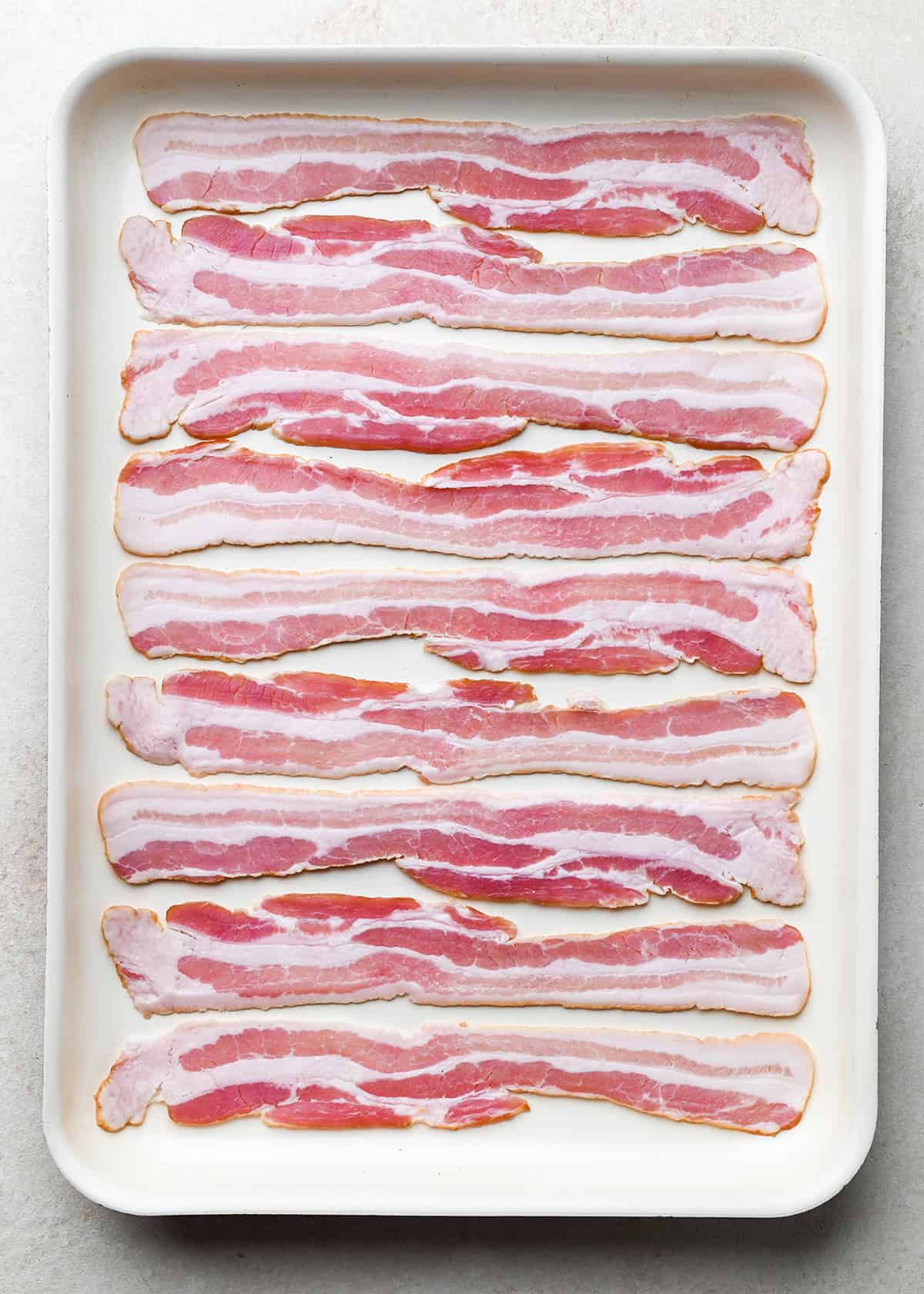 How to Cook Bacon in the Oven - 9 raw pieces of bacon on a baking sheet