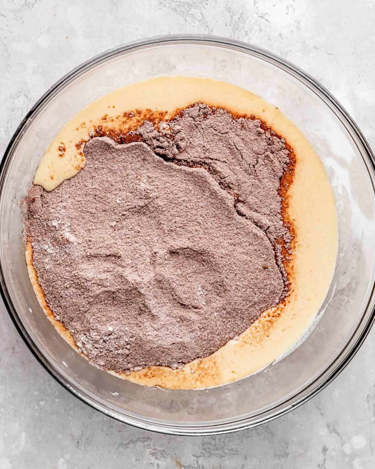 how to make chocolate cake from scratch - dry ingredient mixture added to the wet ingredients in a large glass bowl on a gray surface before mixing