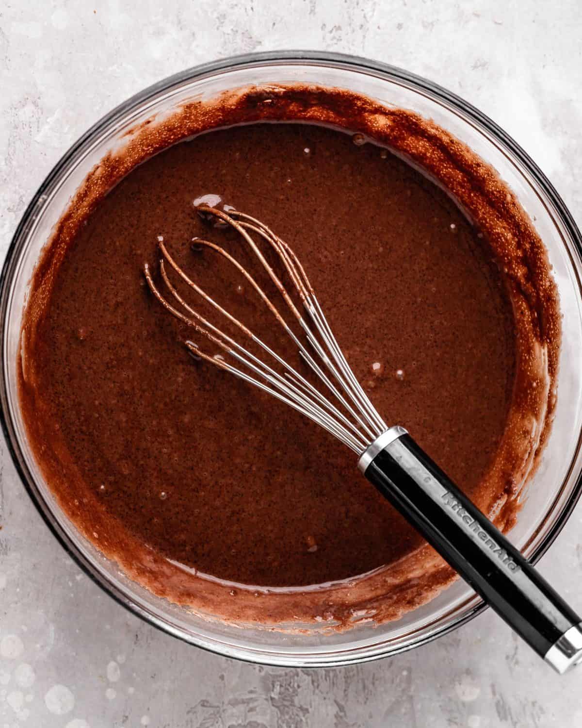 how to make chocolate cake from scratch - cake batter in a large glass bowl with a metal whisk after whisking together.