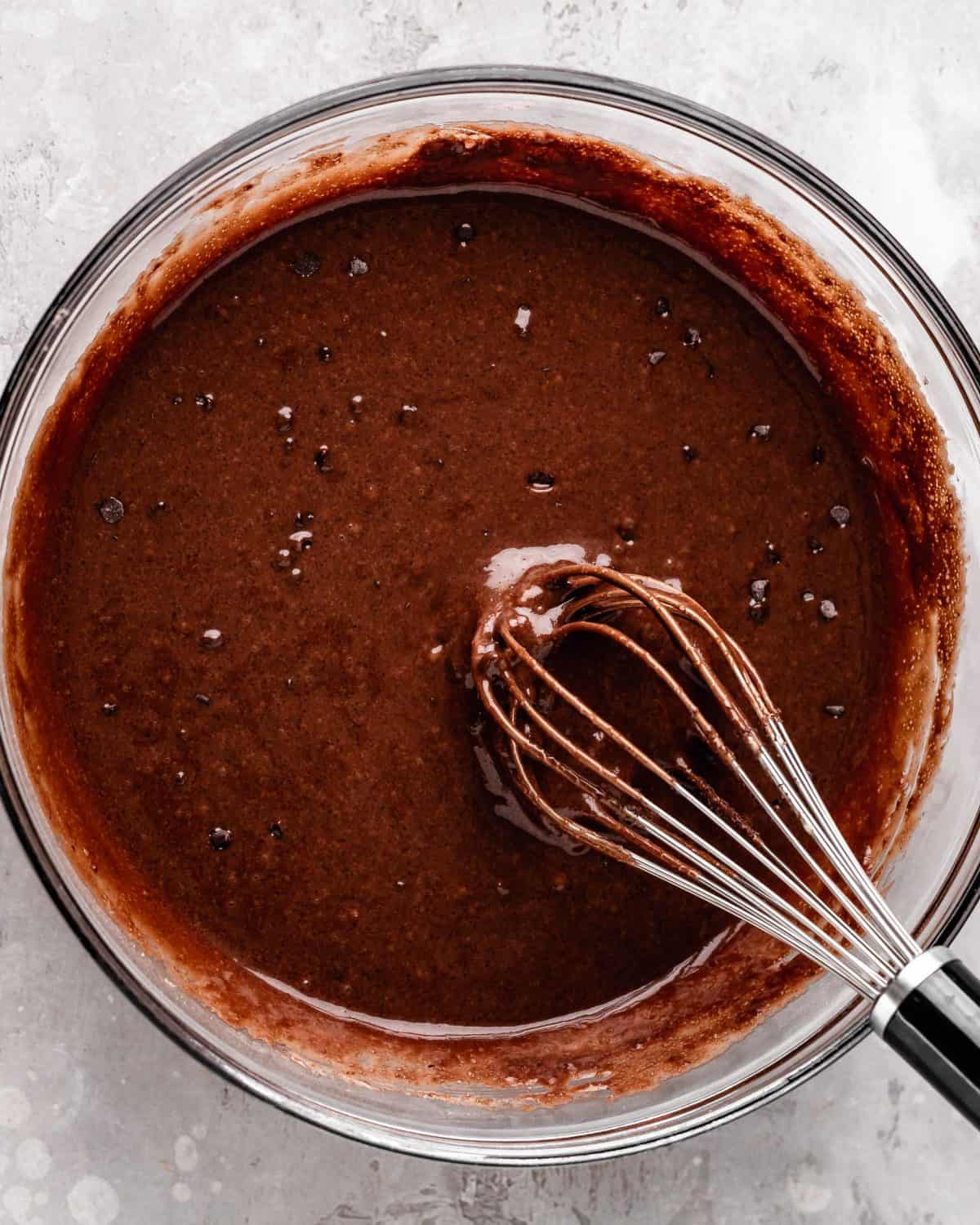 how to make chocolate cake from scratch - final cake batter in a large glass bowl with a metal whisk after whisking in the chocolate chips.