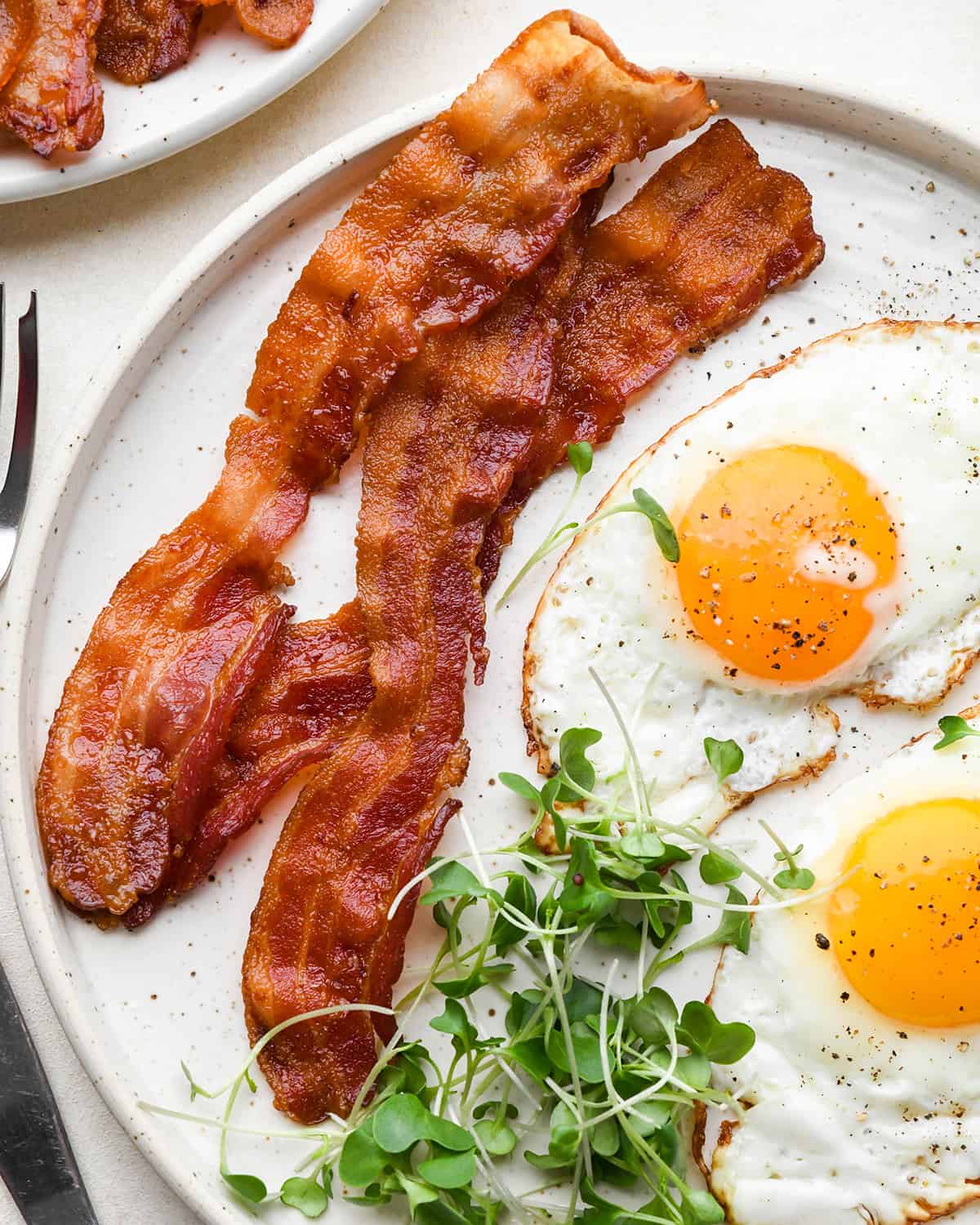 Oven Baked Bacon on a plate with fried eggs and greens
