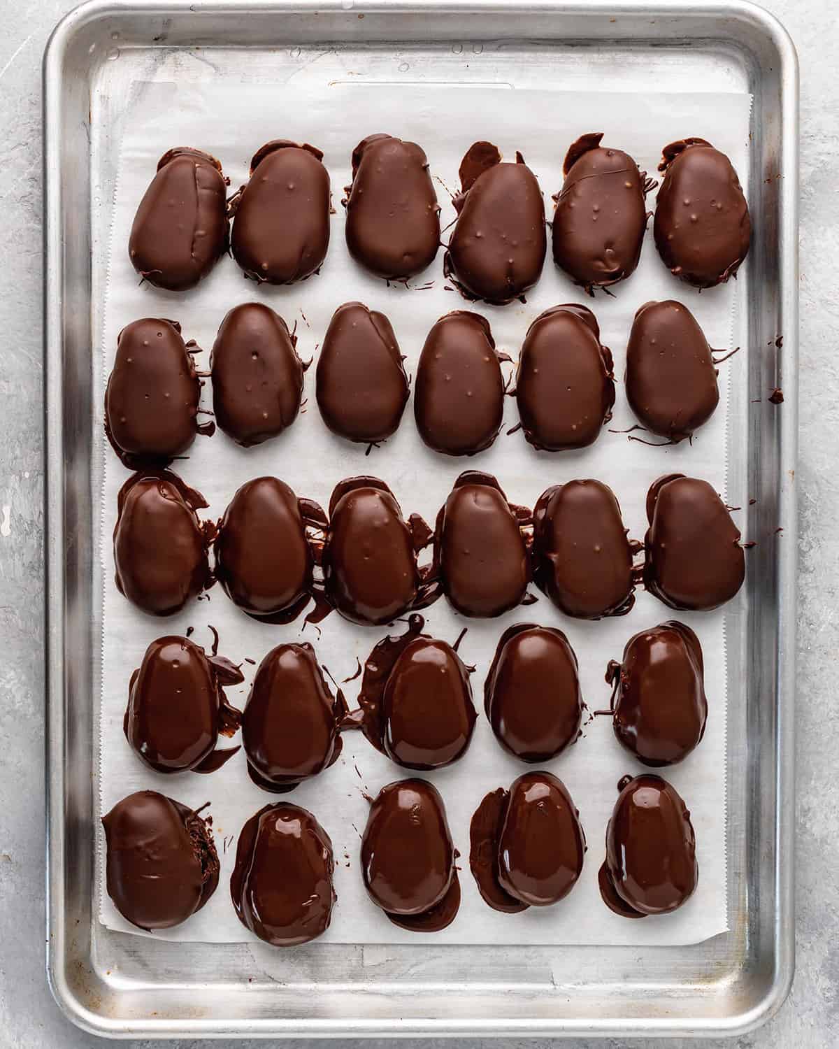 28 peanut butter eggs on a baking sheet right after they've been dipped in chocolate