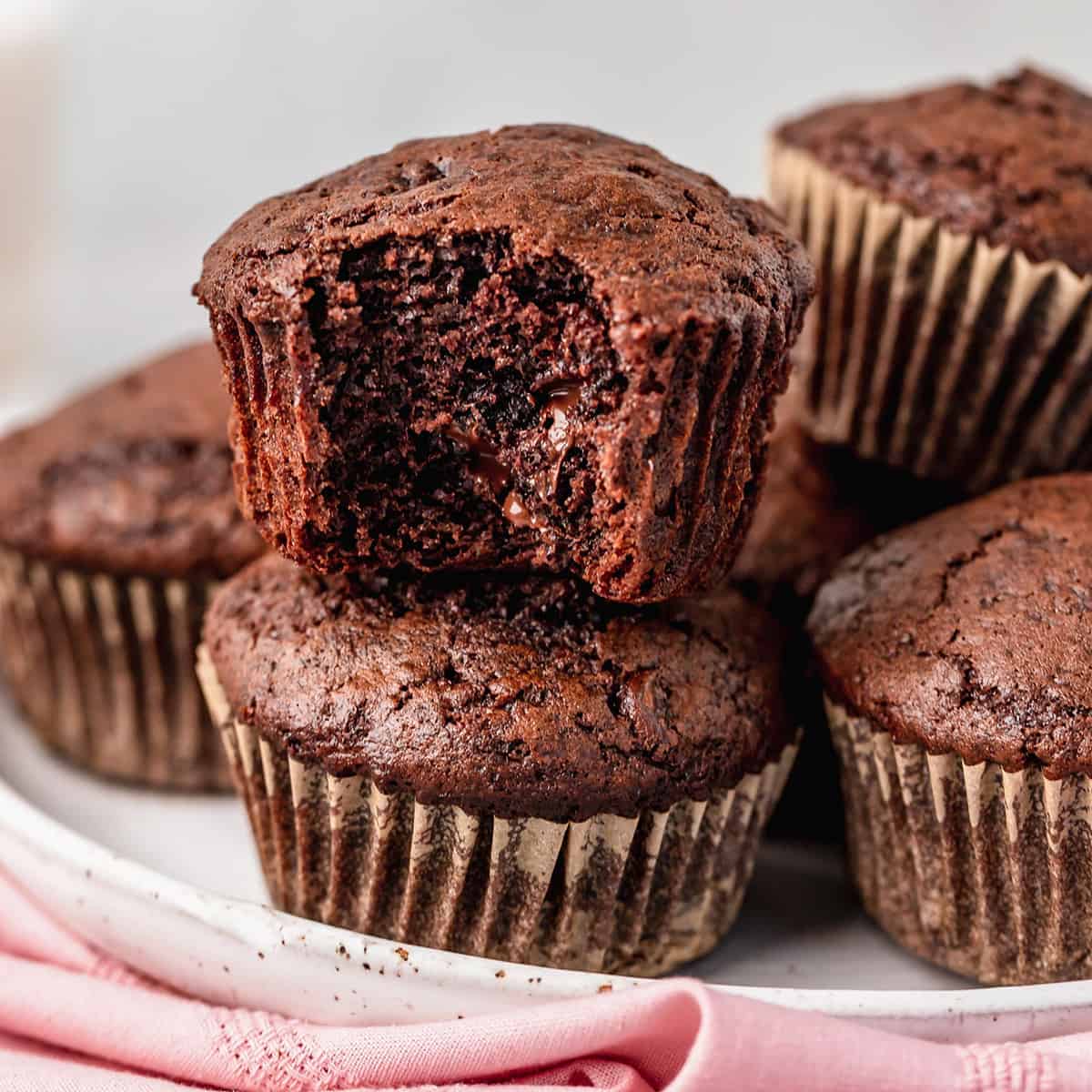a plate of chocolate muffins, one has a bite taken out of it