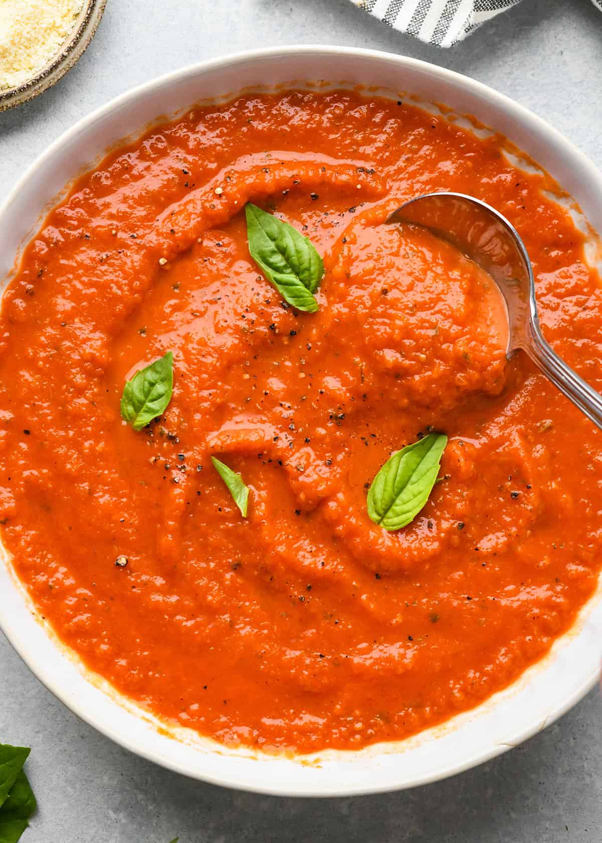 Marinara Sauce Recipe in a bowl with a spoon, garnished with basil