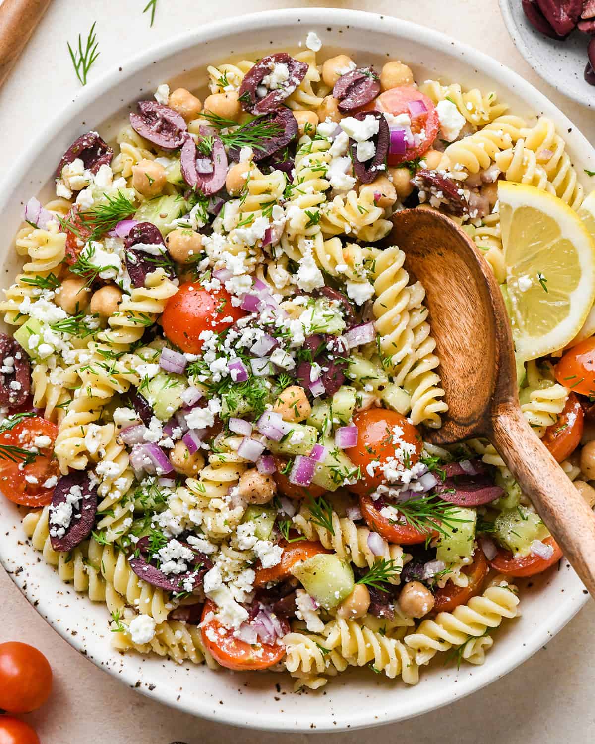 Greek Pasta Salad in a serving bowl with a wooden spoon