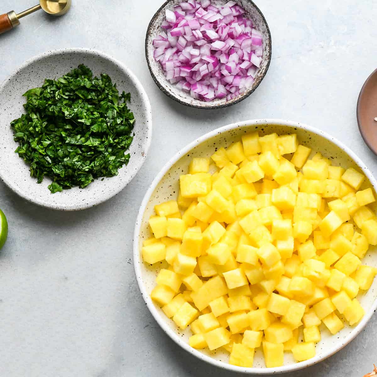 onion, cilantro and pineapple cut up in bowls to make Pineapple Salsa