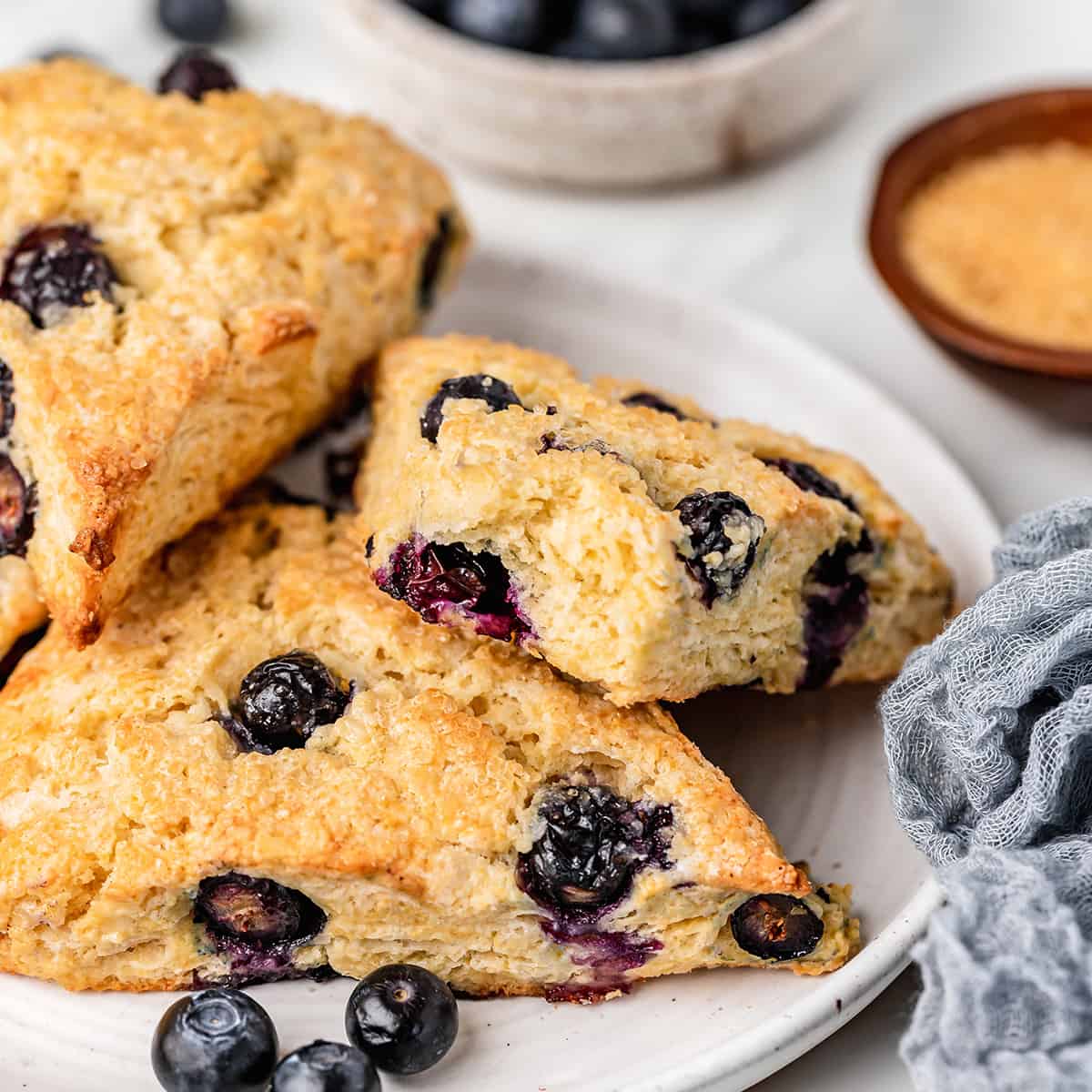 3 Blueberry Scones on a plate, one has a bite taken out of it