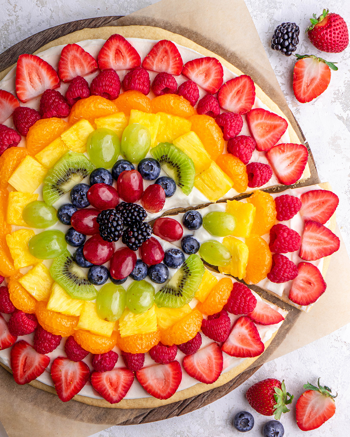 Fruit Pizza on a serving plate with one slice cut out of it 