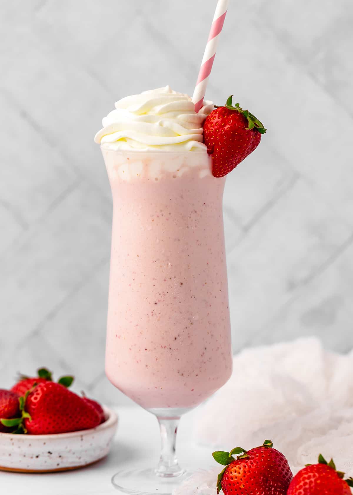 Strawberry Milkshake in a glass with a straw, whipped cream and a strawberry