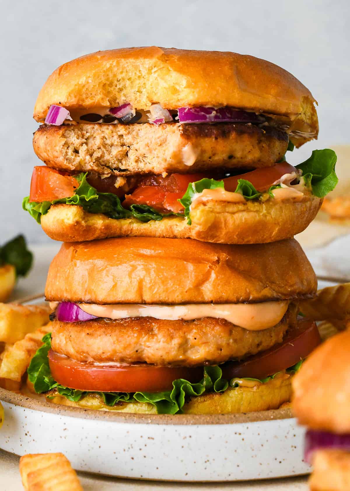 a stack of 2 Turkey Burgers on buns, the top one has a bite taken out of it