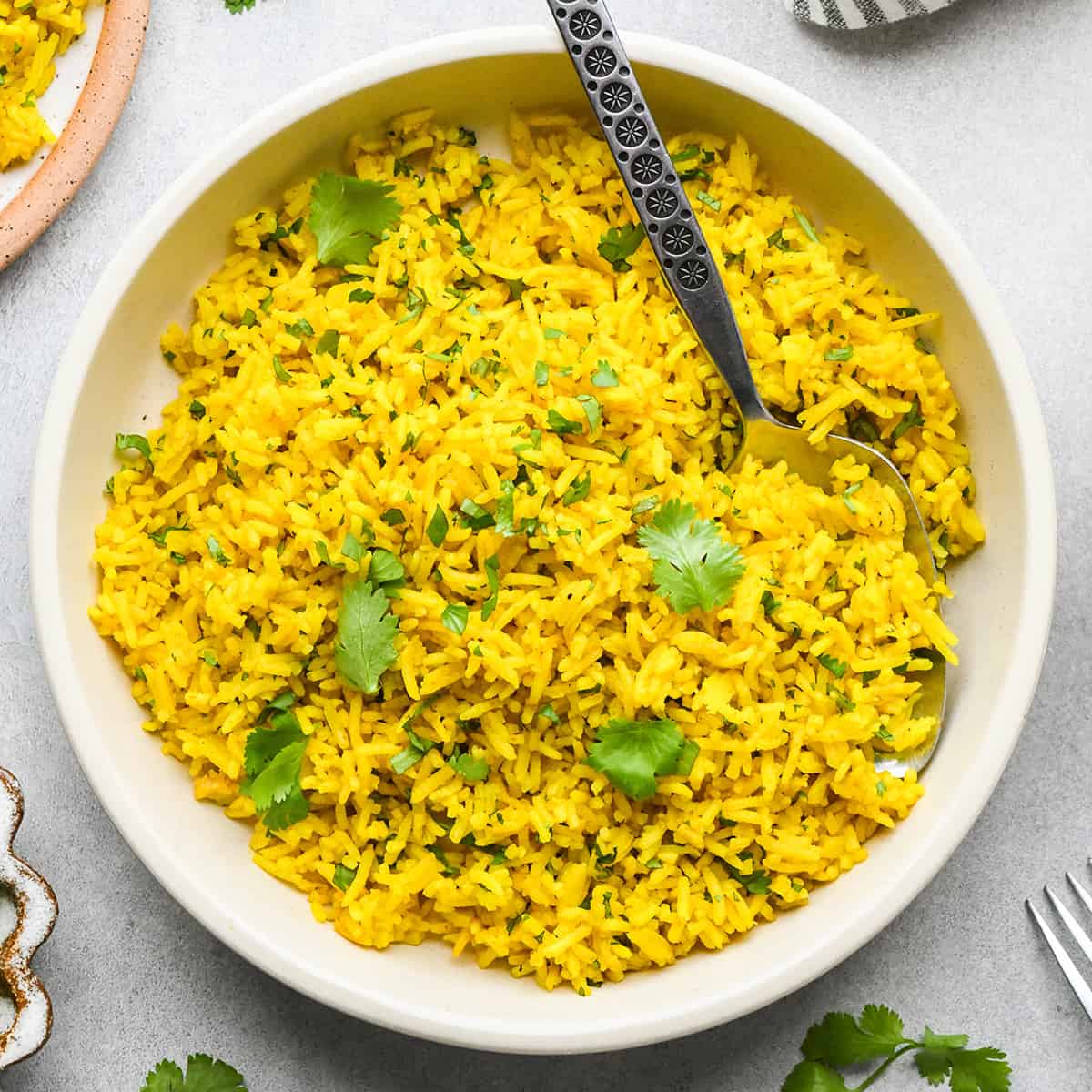 a bowl of Turmeric Rice garnished with cilantro with a spoon in it