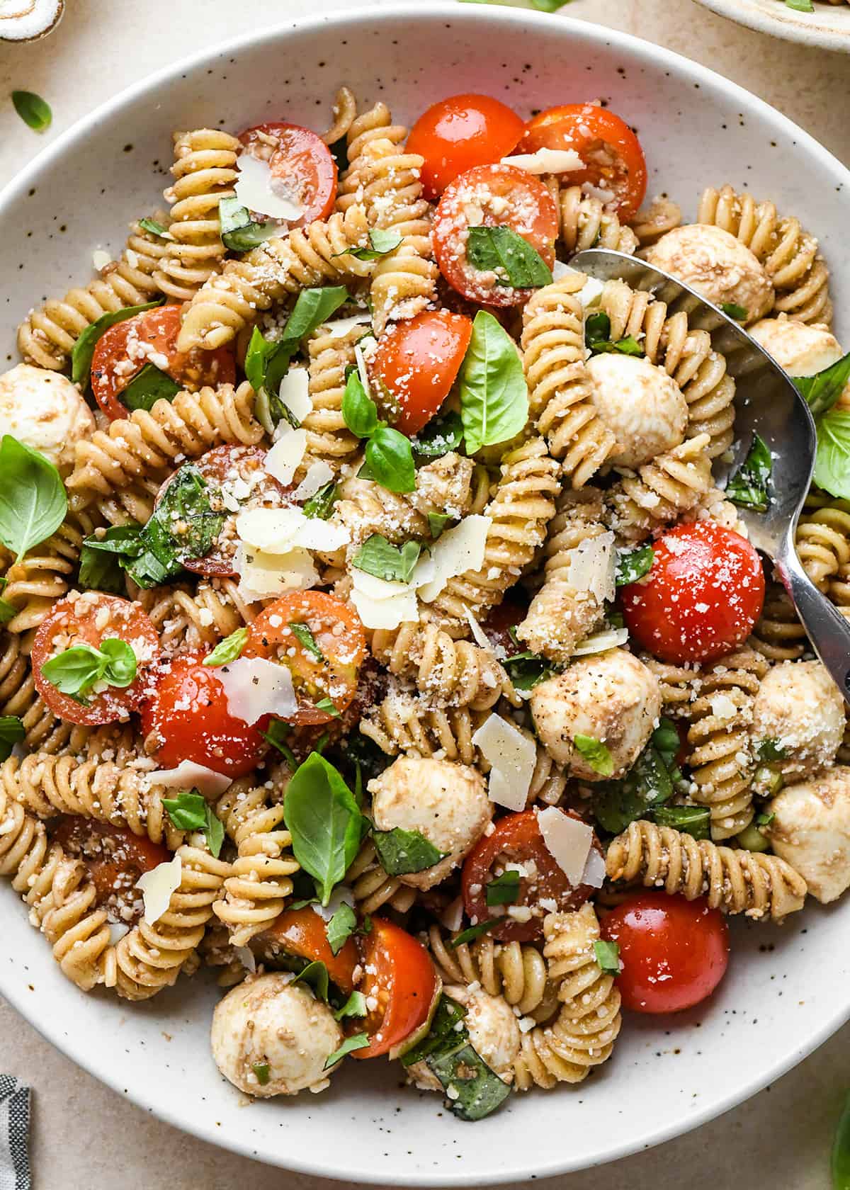 Caprese Pasta Salad in a bowl with a spoon garnished with fresh basil and parmesan cheese