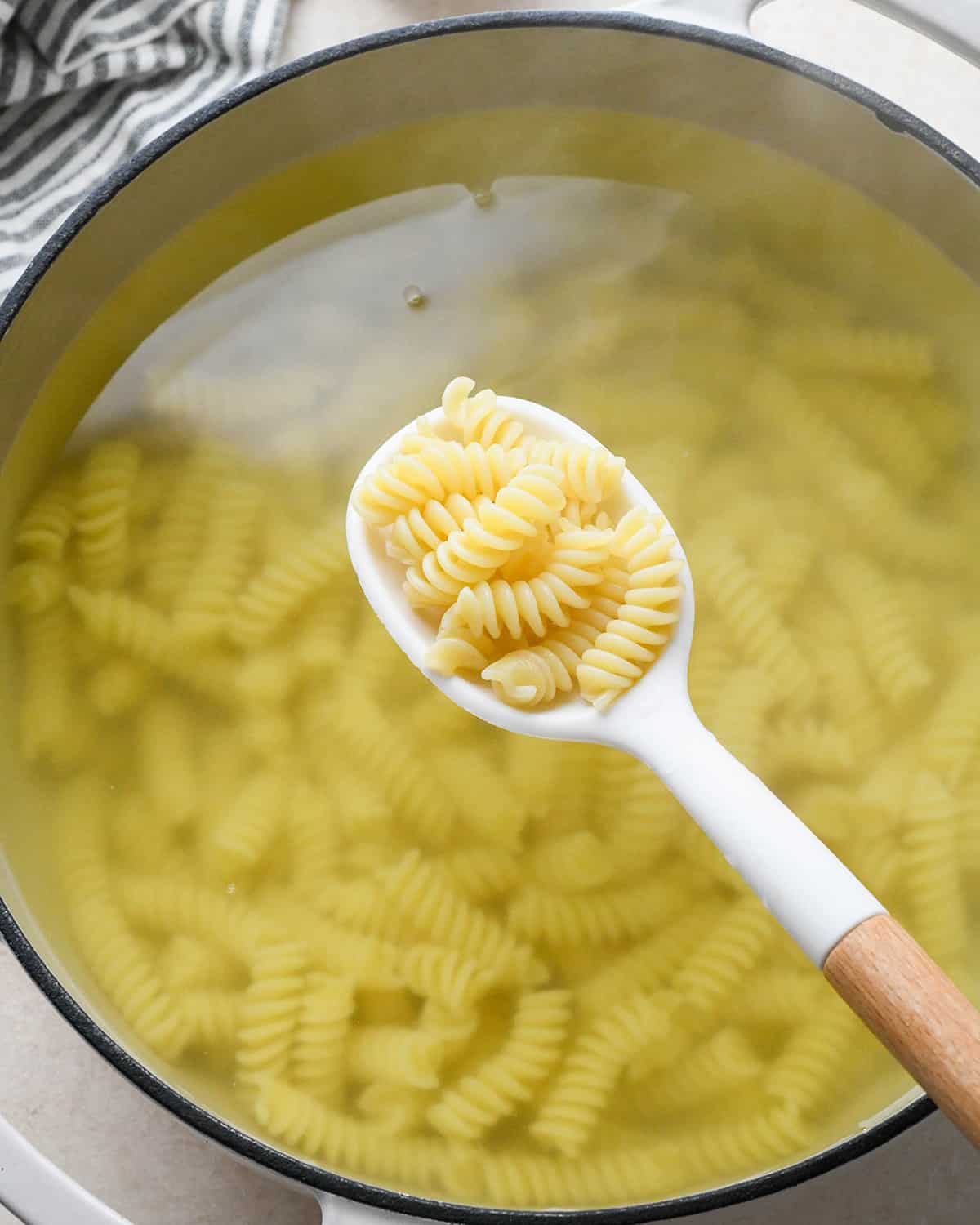 a spoon holding cooked pasta over a pot