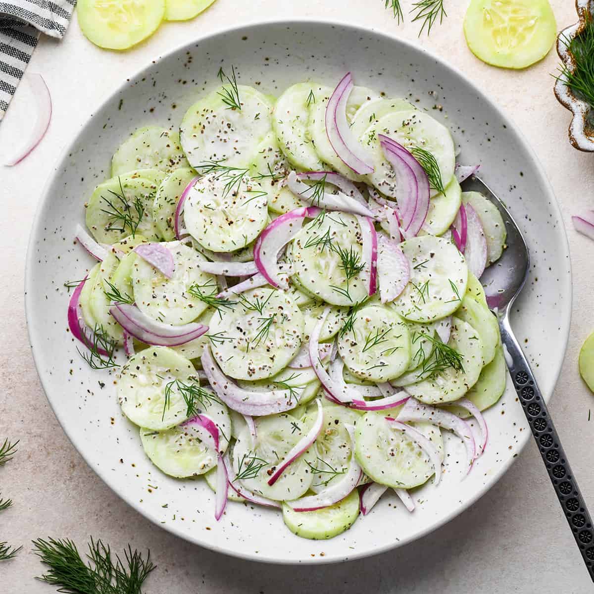 Cucumber Salad garnished with fresh dill in a bowl with a spoon