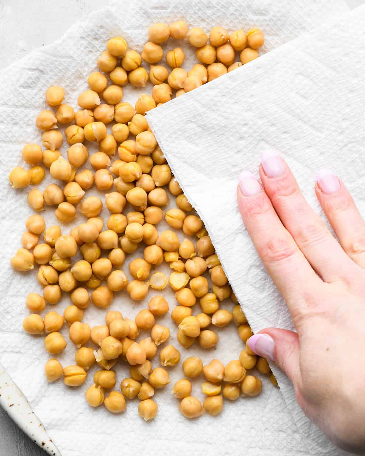making roasted chickpeas recipe - a hand drying drained chickpeas on a paper-towel lined white ceramic plate with a paper towel