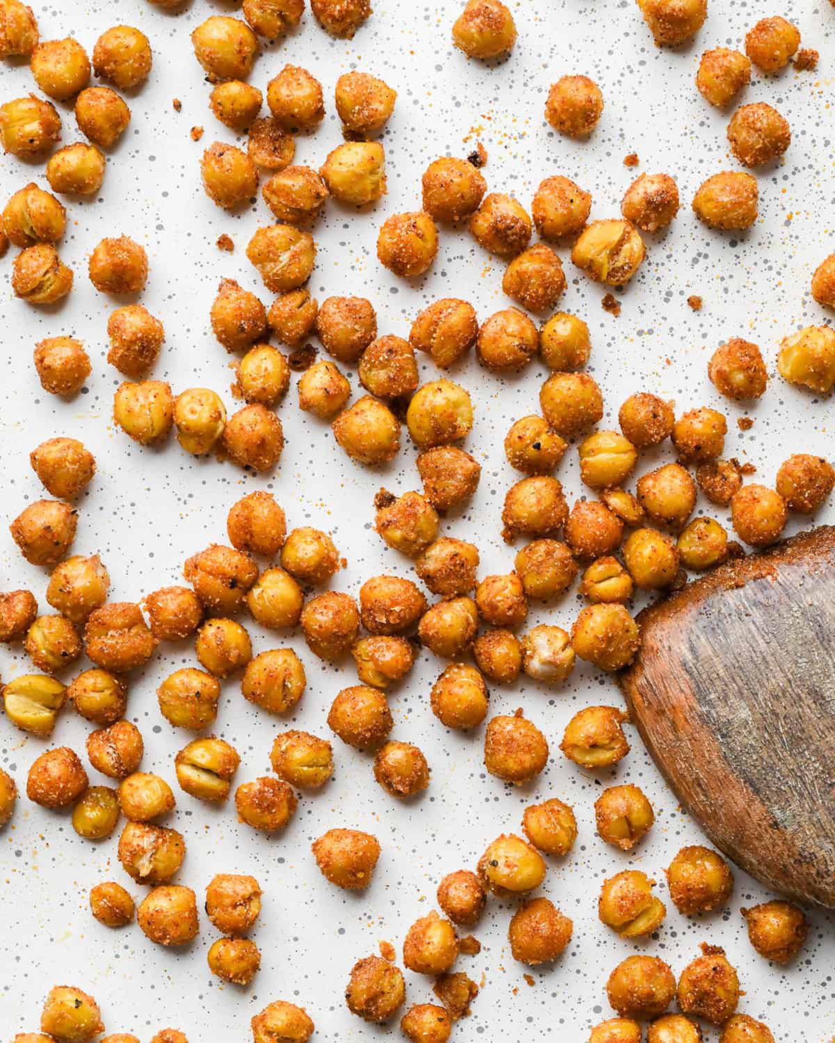 making roasted chickpeas recipe - roasted chickpeas on a white baking sheet with a wooden spatula
