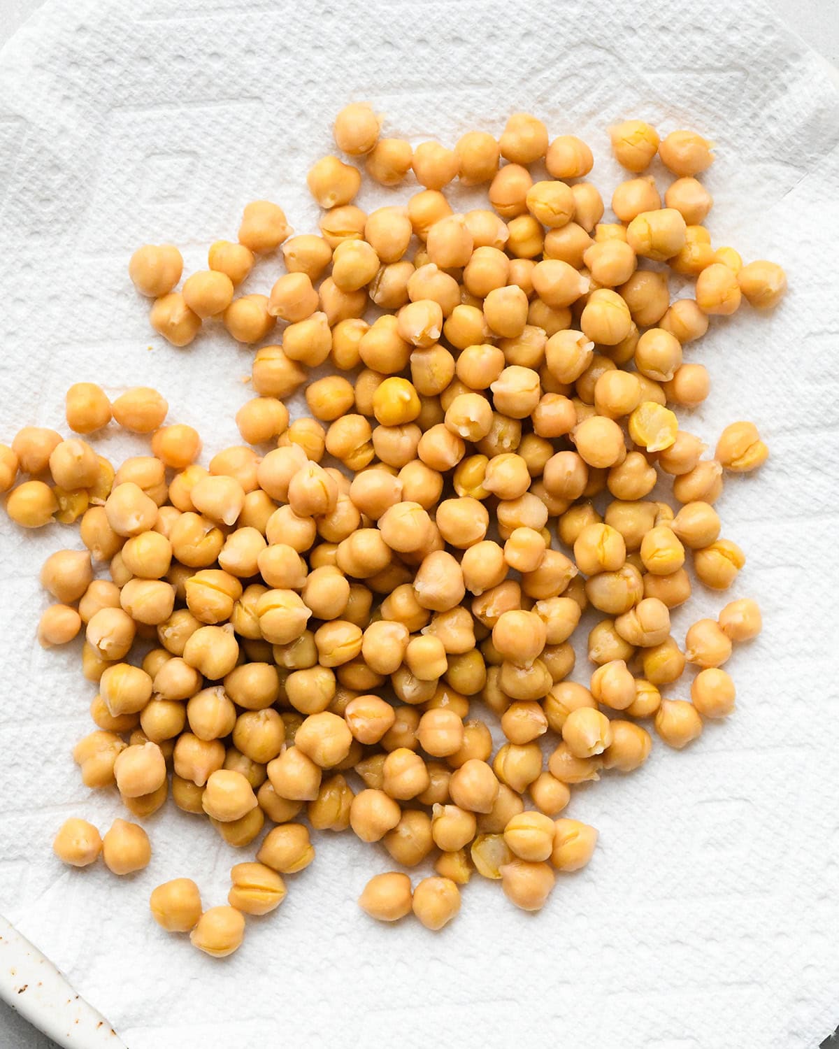 making roasted chickpeas recipe - drained chickpeas on a paper-towel lined white ceramic plate