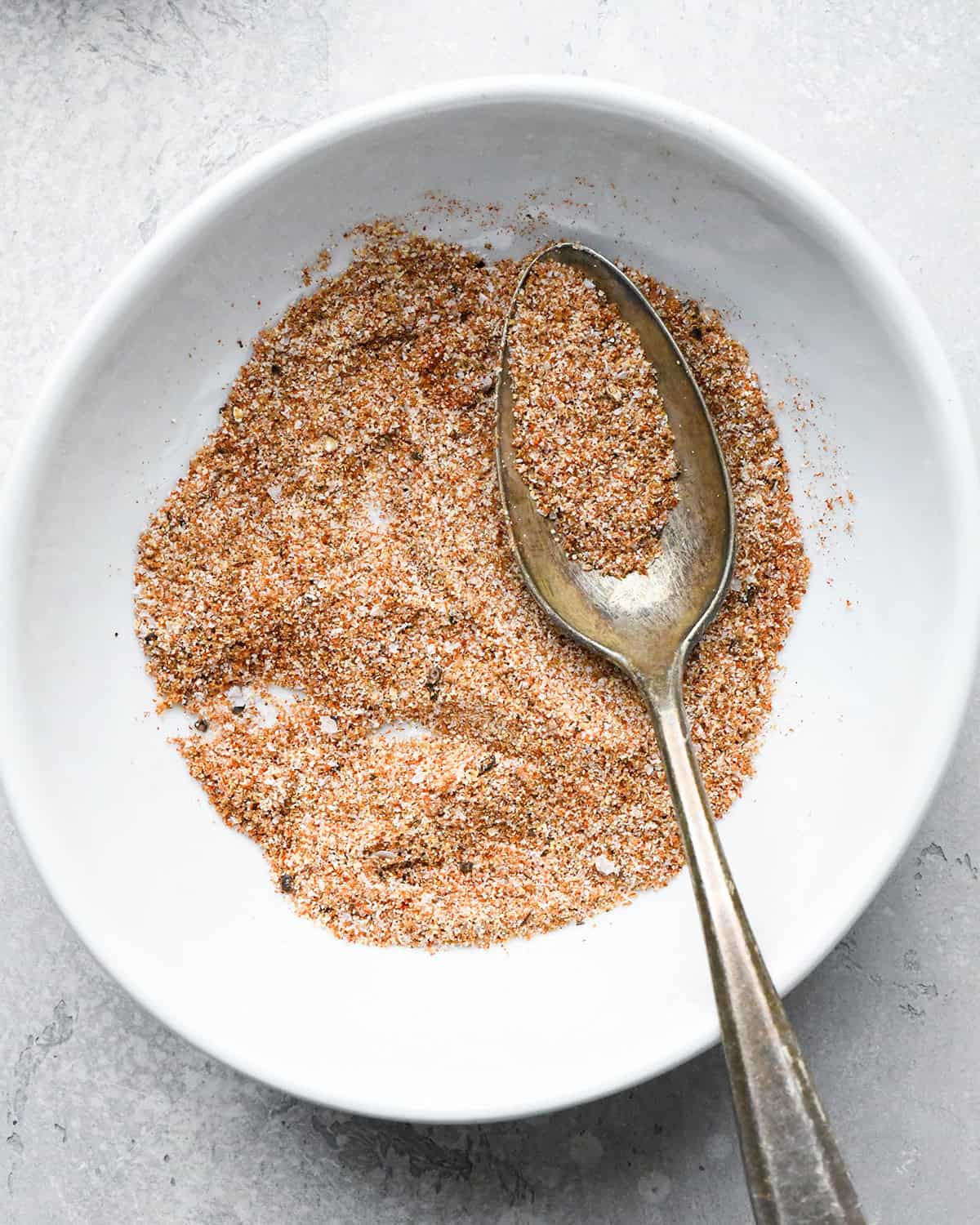 making roasted chickpeas recipe - spice mixture after being stirred in a small white bowl with a metal spoon in the bowl with some of the spice mixture on it