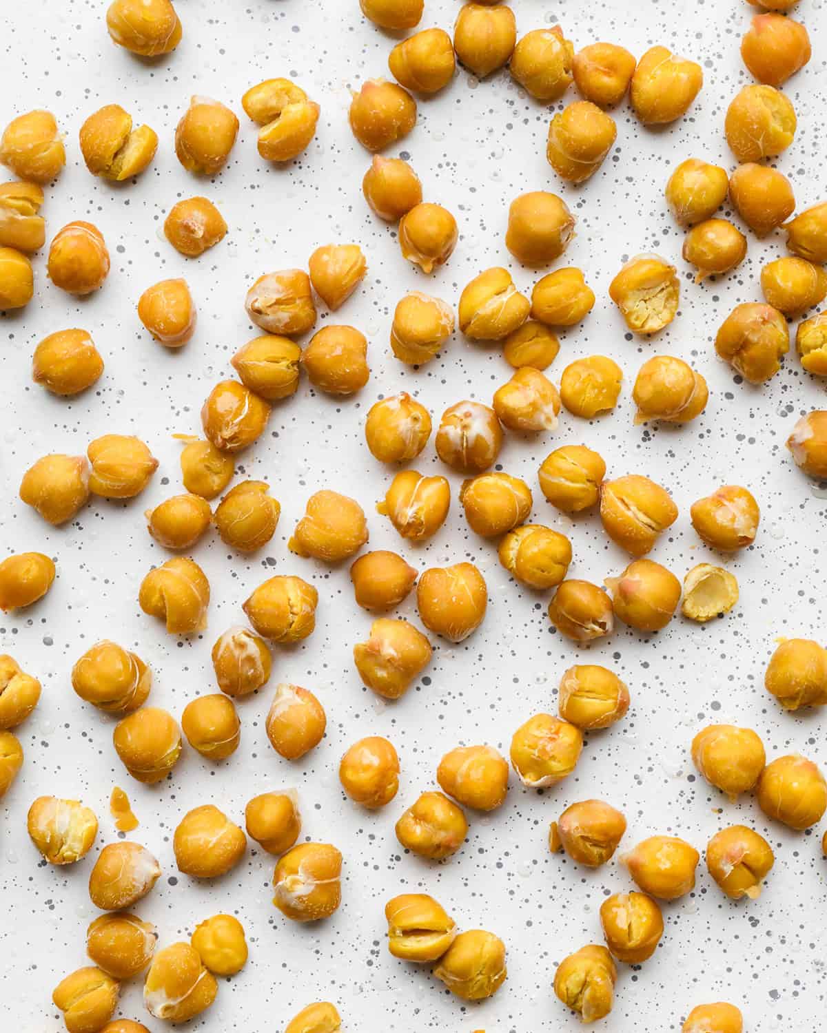 making roasted chickpeas recipe - chickpeas on a white baking sheet after being roasted for 15 minutes