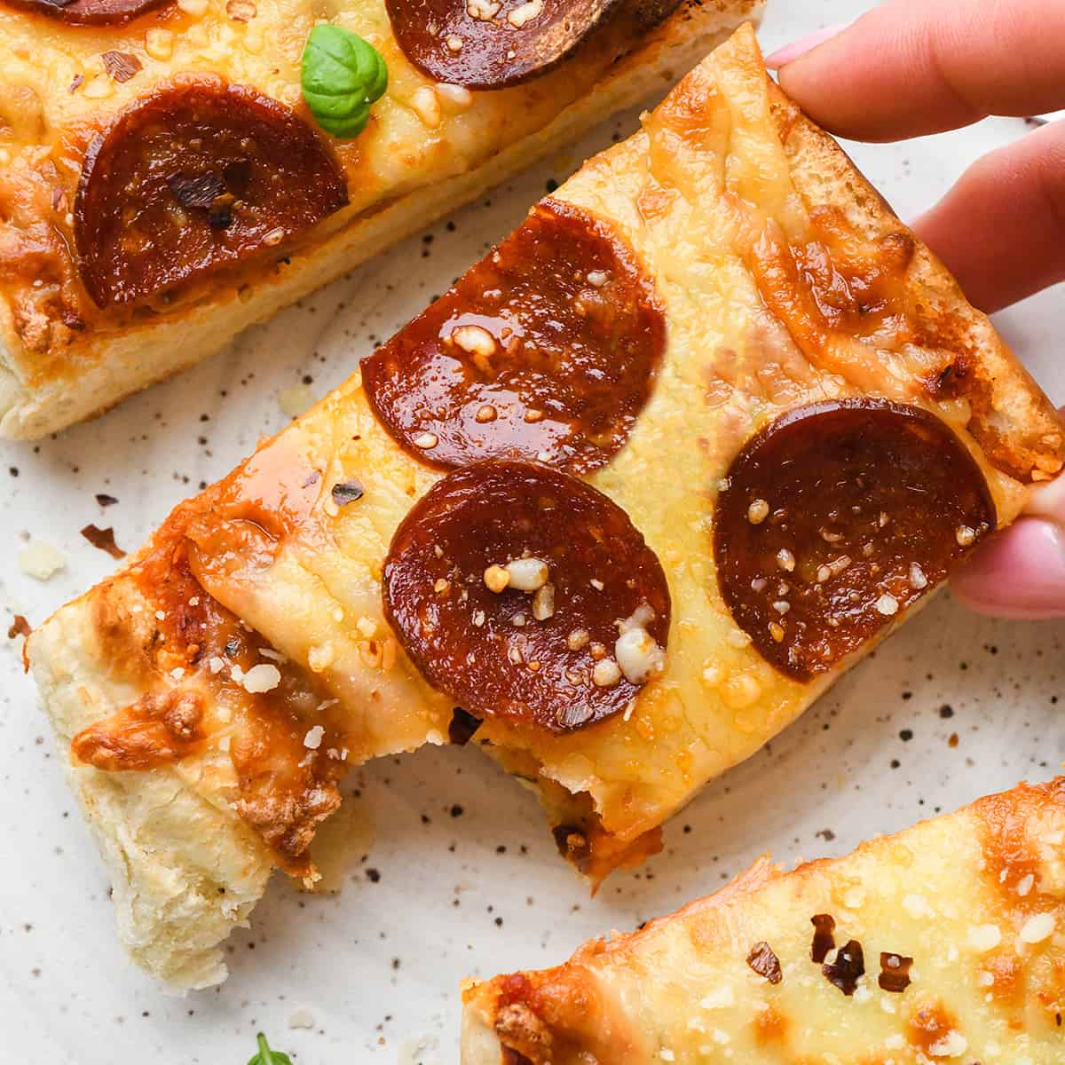 a hand holding a piece of French Bread Pizza with a bite taken out of it