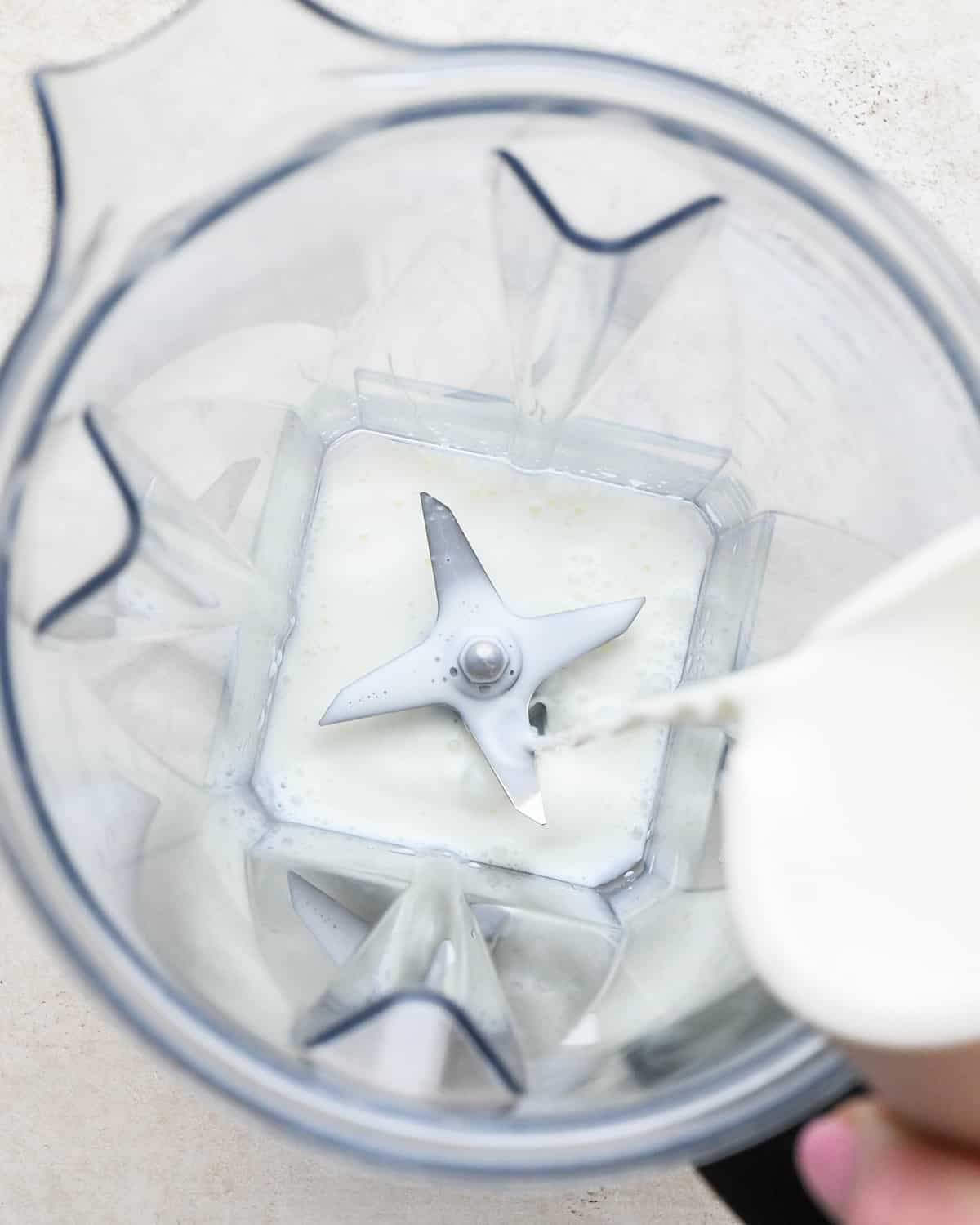 milk being poured into a blending container to make a Vanilla Milkshake