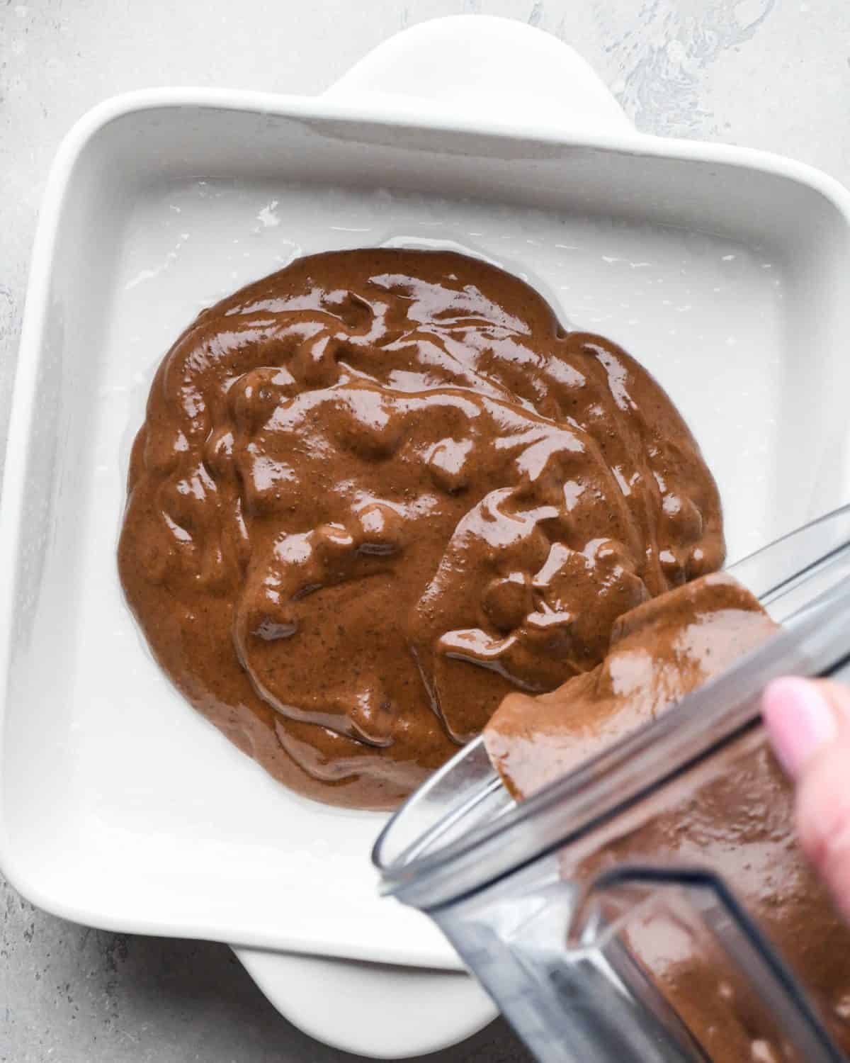 black bean brownies batter being poured from the blending contianer into a white ceramic baking dish