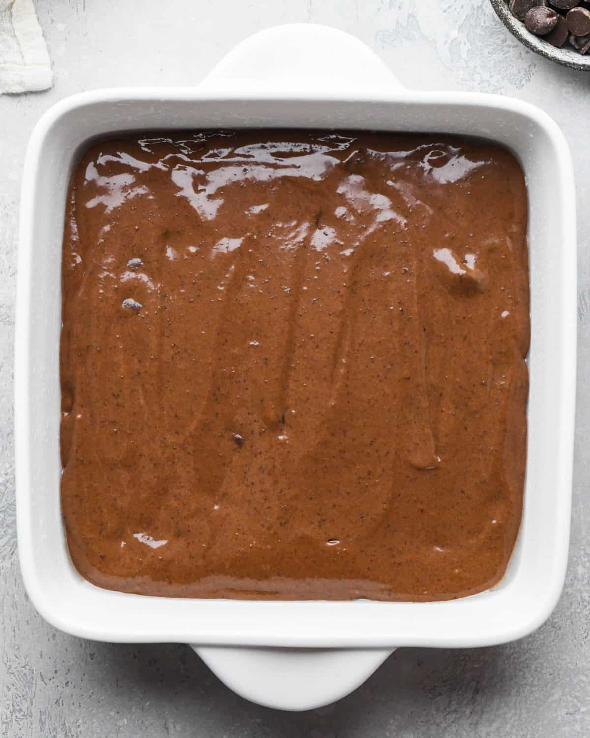 black bean brownies batter spread evenly into a white ceramic square baking dish before baking