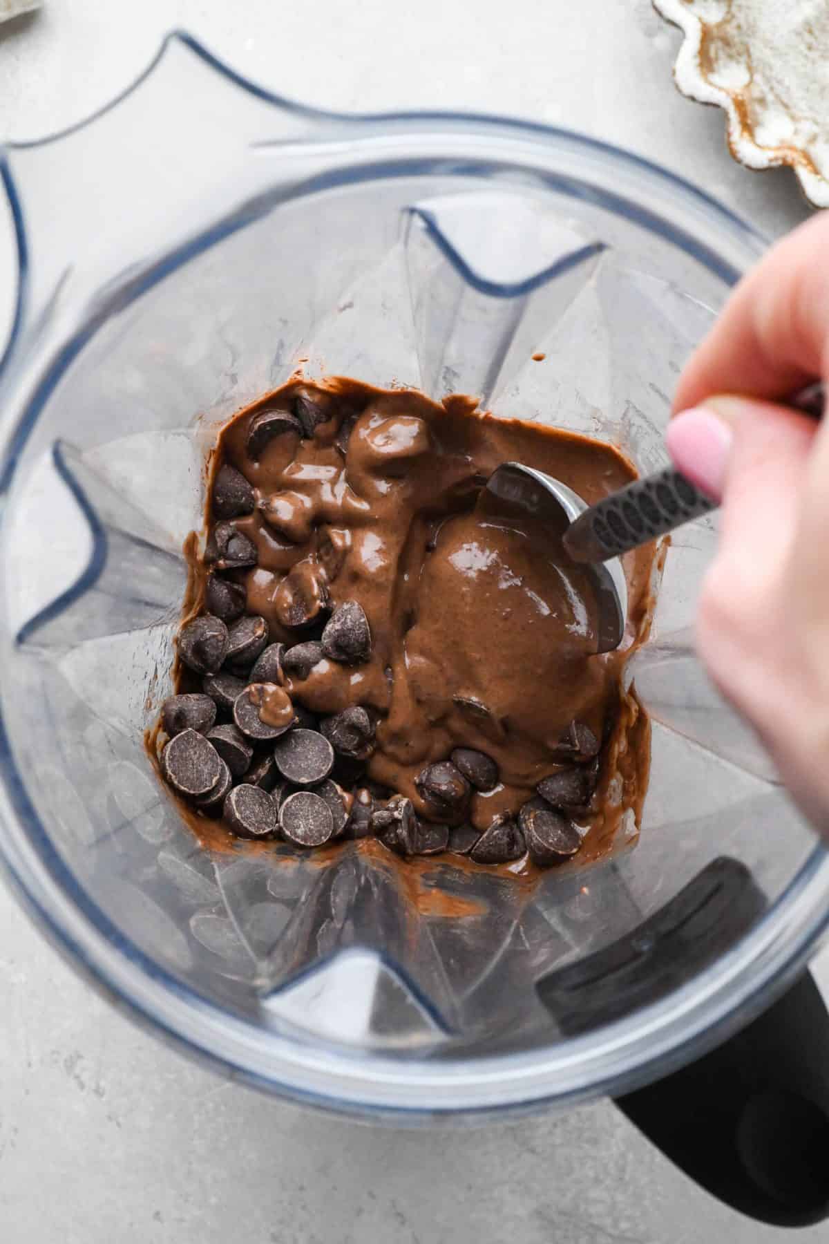 making black bean brownies - chocolate chips being stirred into the batter in a blending container with a metal spoon