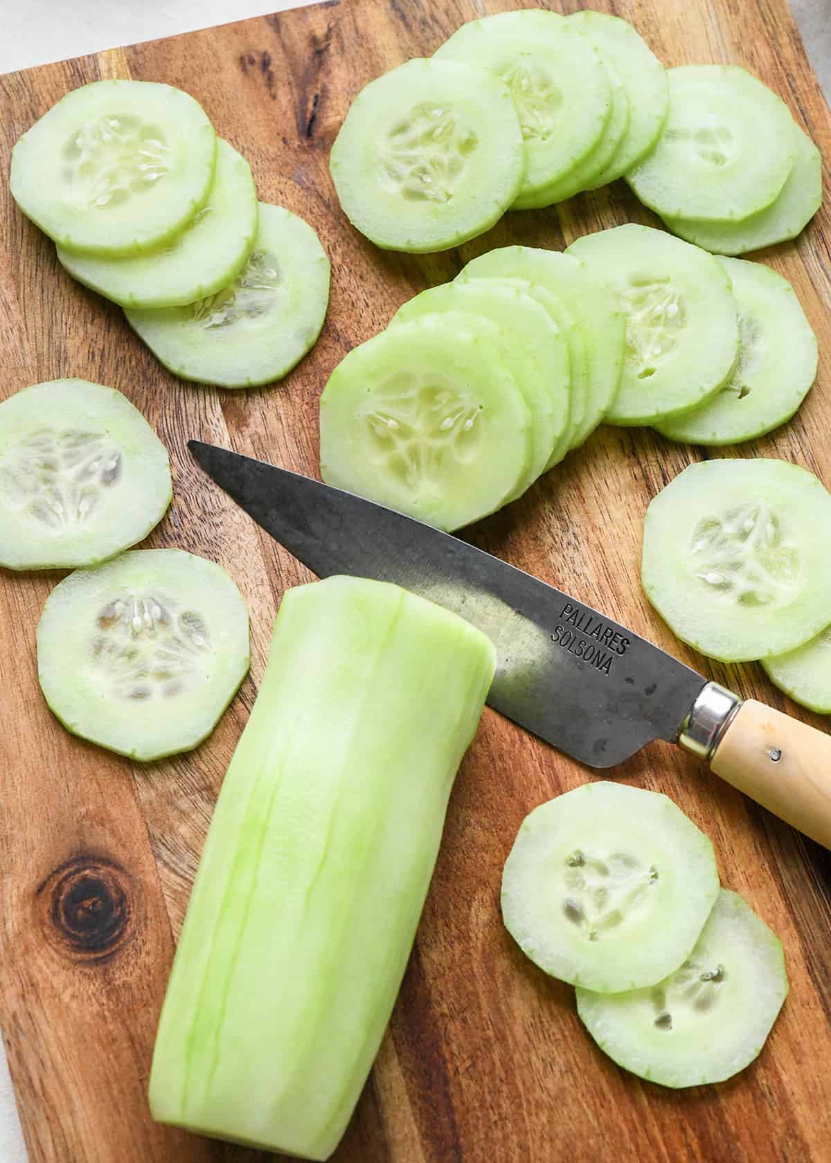 cucumbers being thinly sliced on a cutting board with a knife