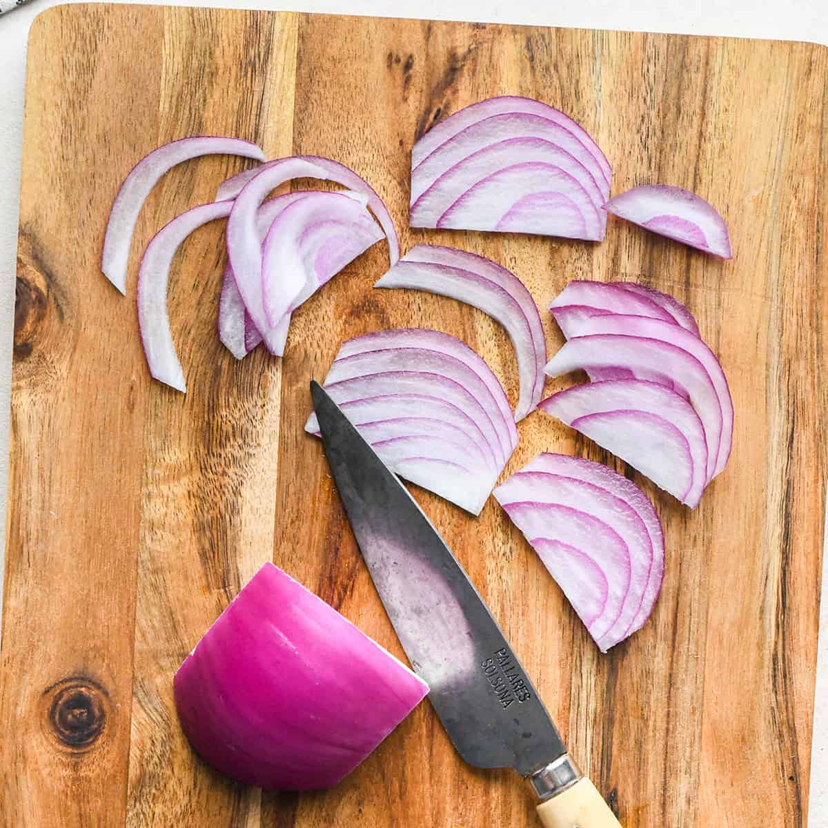 red onions being thinly sliced on a cutting board ot make cucumber salad