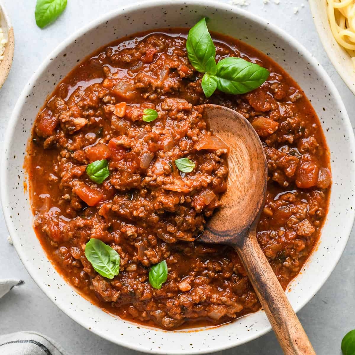 a bowl of Spaghetti Meat Sauce with a wooden spoon and basil