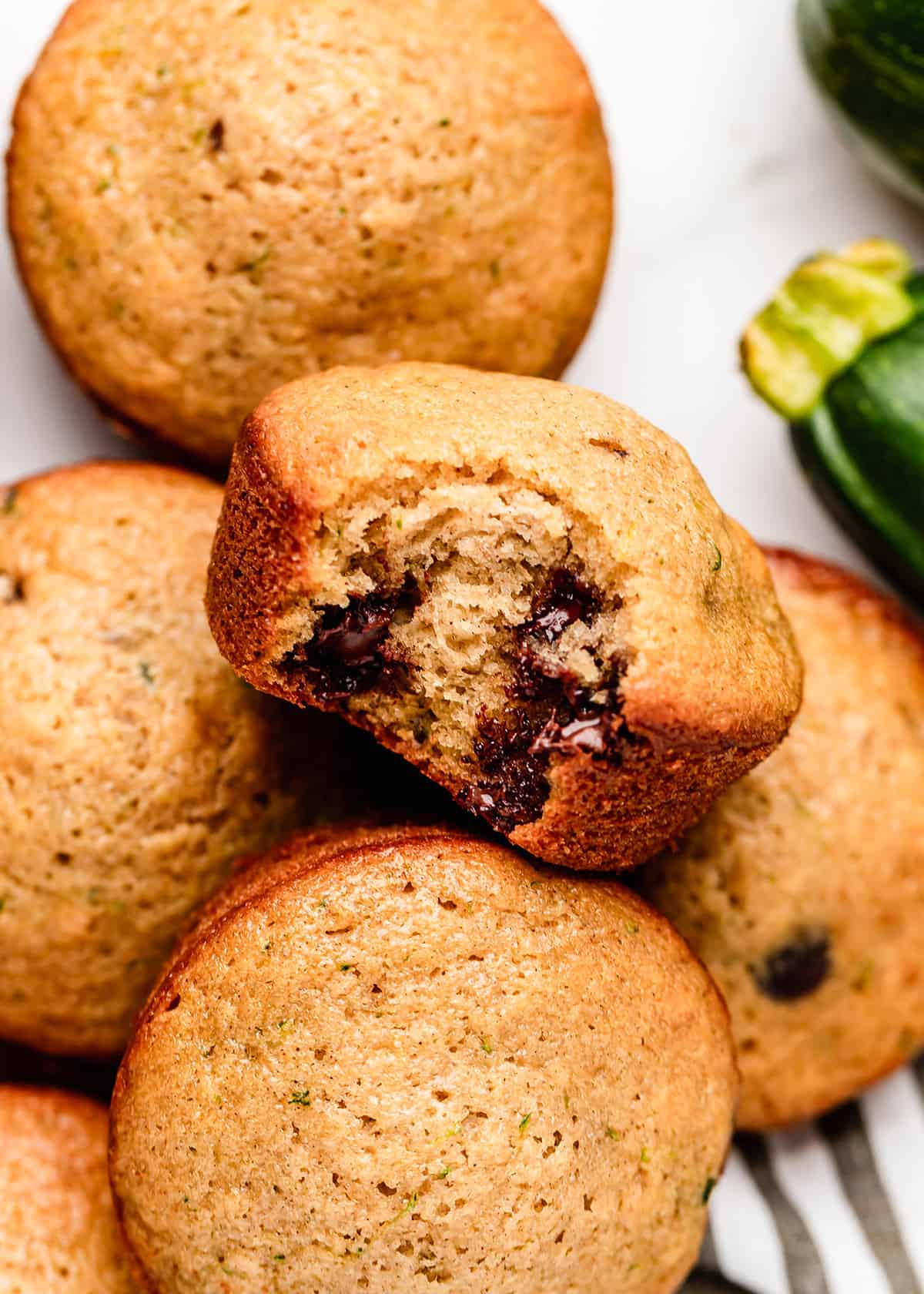 5 Zucchini Chocolate Chip Muffins, one with a bite taken out of it