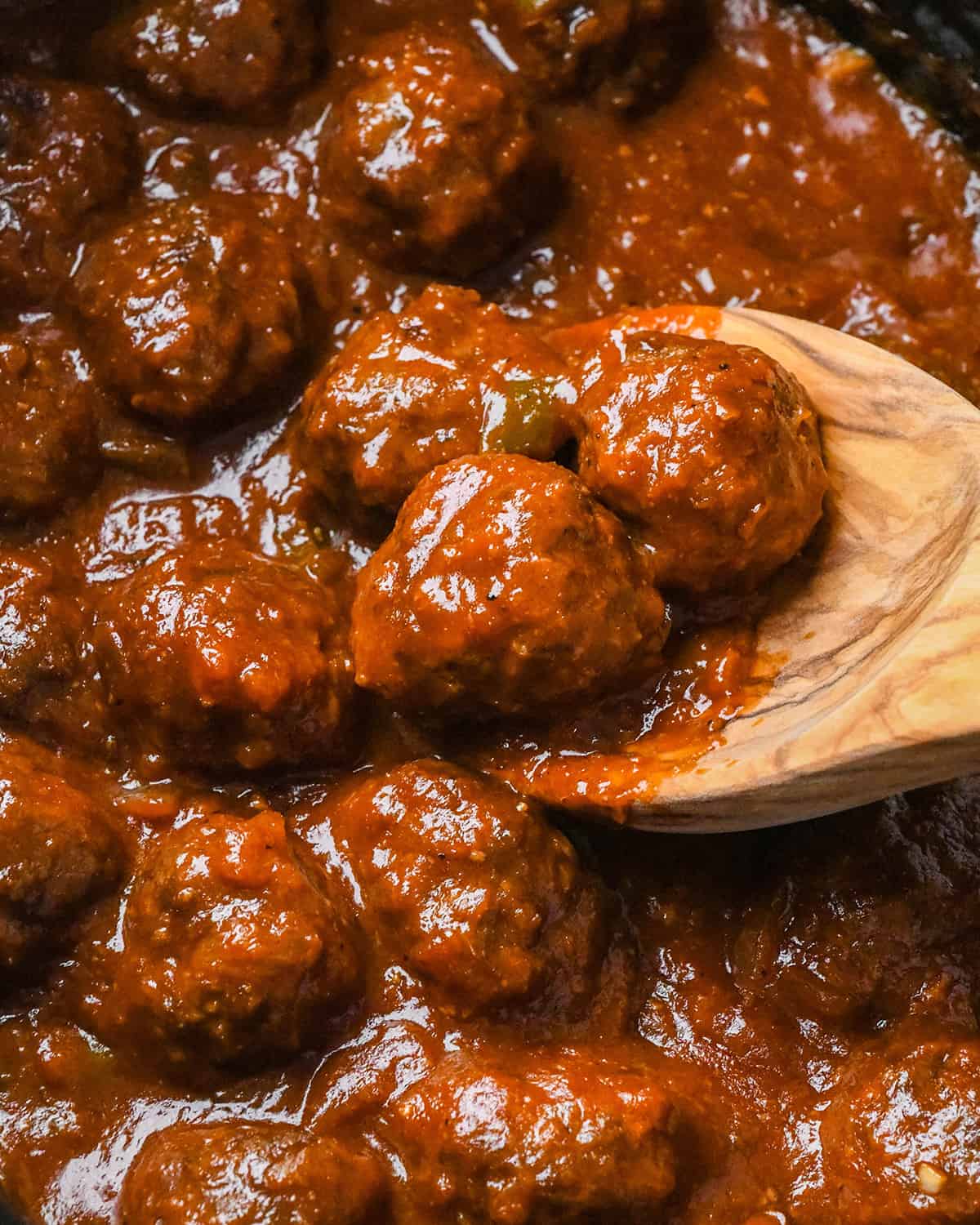 a wooden spoon scooping BBQ Meatballs out of a crockpot