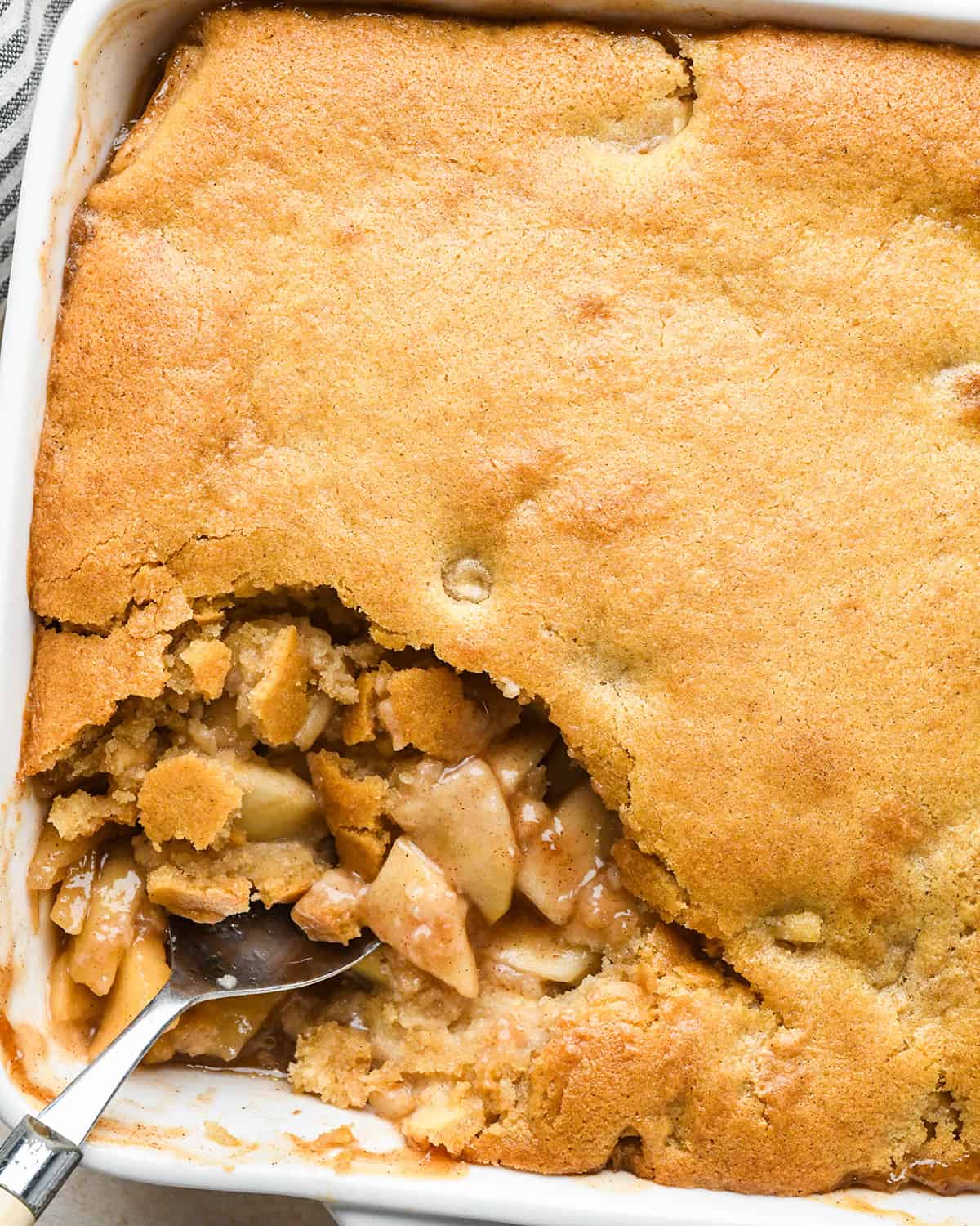 Apple Cobbler in a baking pan with a spoon scooping some out 