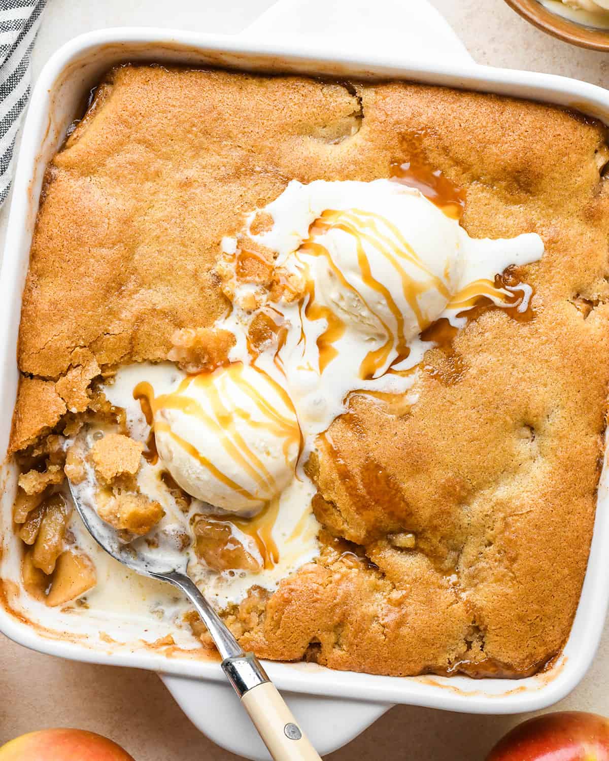 Apple Cobbler in the baking pan with vanilla ice cream, caramel sauce and a spoon